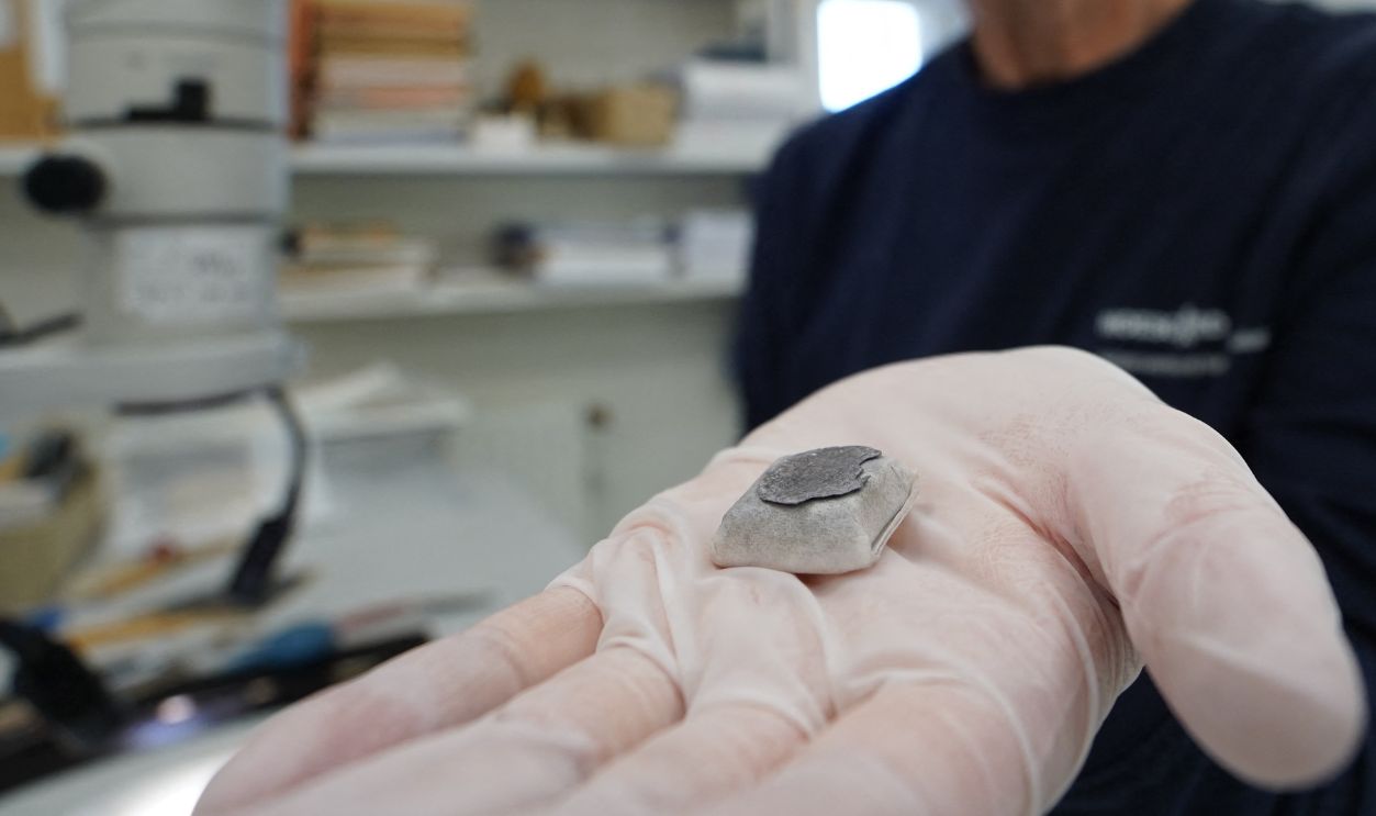 Getty Images - 2219839323 - Conservator Helle Strehle holds a Viking Age silver coin discovered at a Viking Age burial site in Lisbjerg, a village seven kilometres north of Aarhus, Denmark's second largest city, on June 13, 2025. Some 30 richly adorned 10th-century graves, which experts believe belonged to a noble family, have been discovered in northern Denmark, a museum announced on June 17, 2025. Pearls, coins, ceramics, and a box containing a gold thread -- objects deemed "spectacular" by experts -- were accidentally unearthed during construction work.