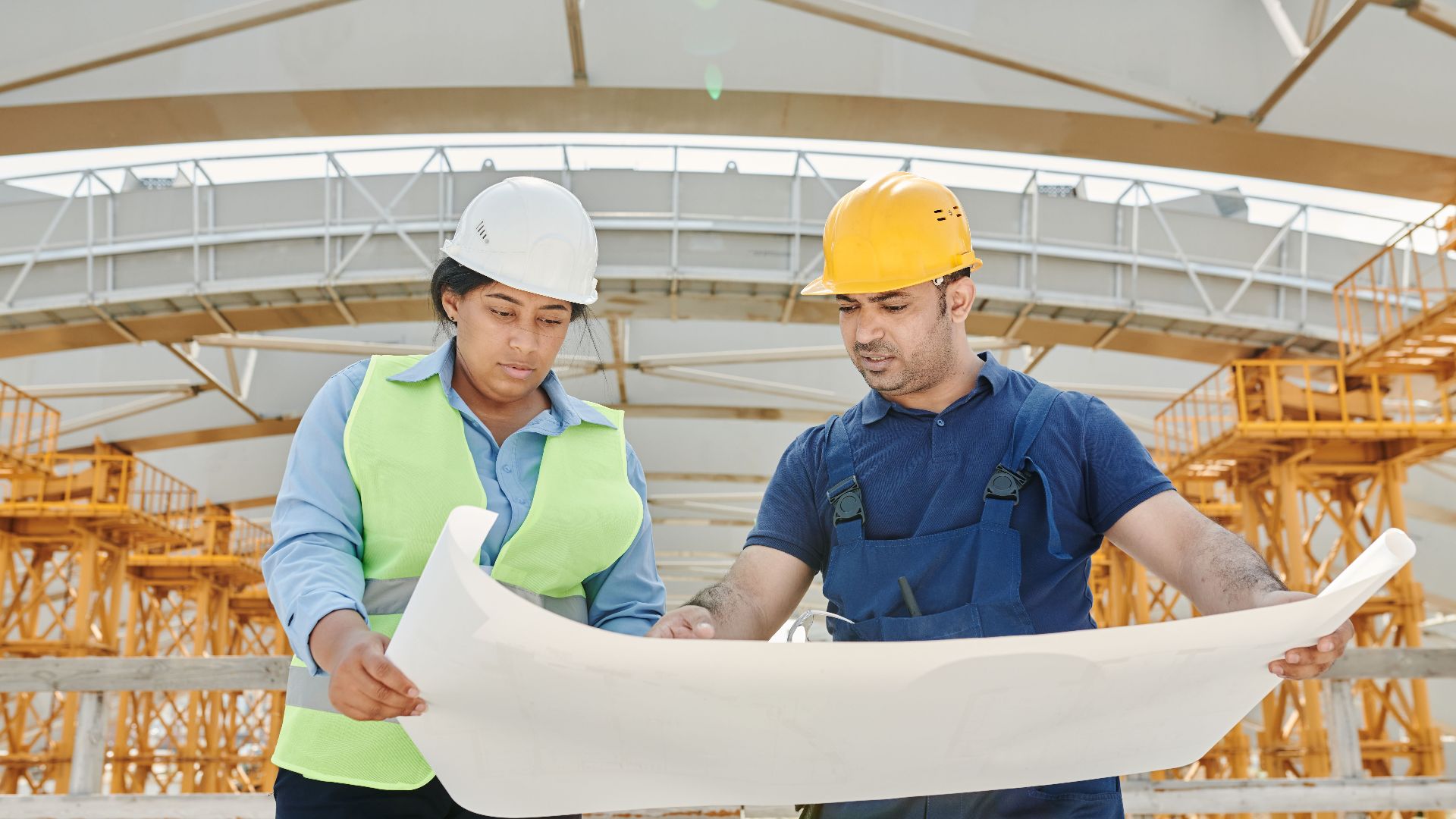 Male and female engineers discussing blueprints at a construction site, promoting teamwork and planning.
