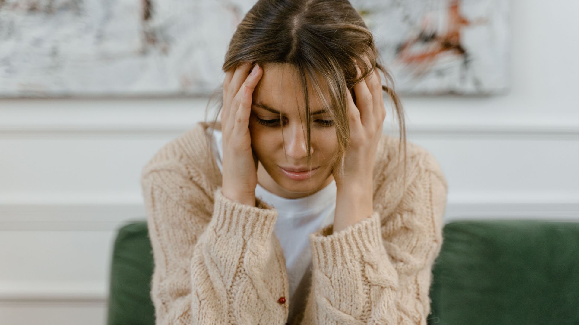 A woman sitting on a sofa holding her head, expressing stress and frustration indoors.