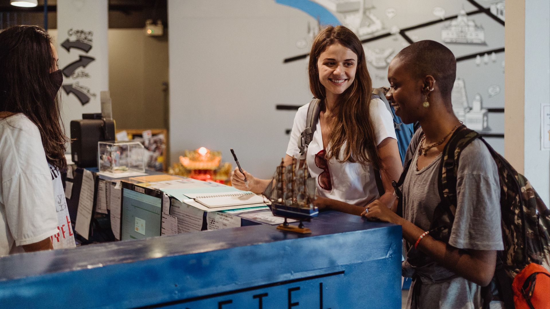 Three travelers checking into a hostel at the reception desk, showcasing hospitality and adventure.