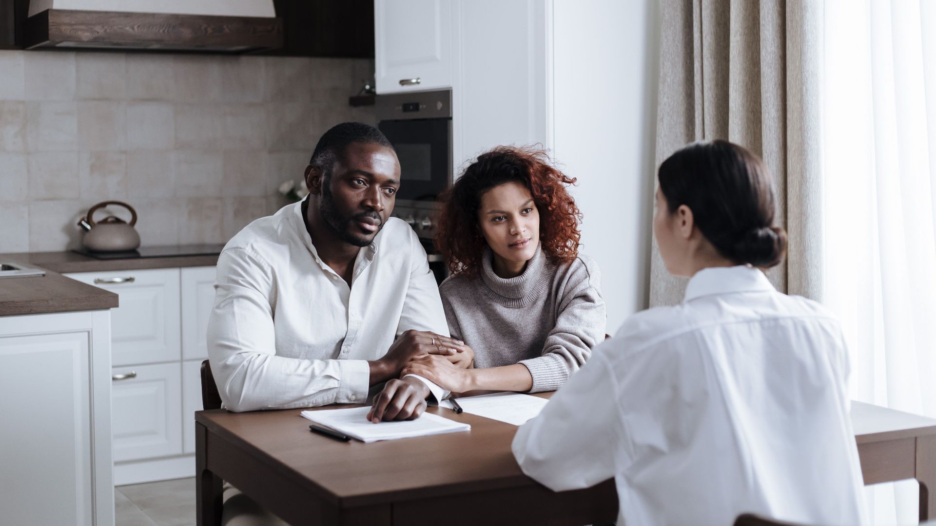 A couple discusses adoption with a social worker in a modern kitchen setting.