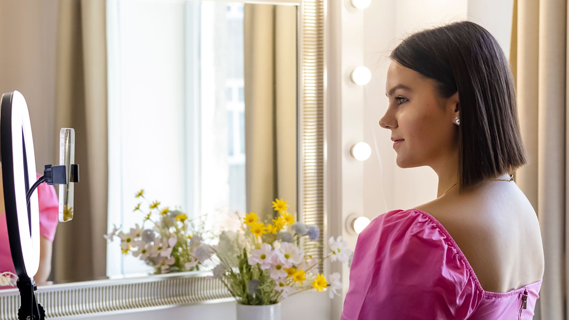 A young woman records a vlog using a ring light in front of a stylish mirror.