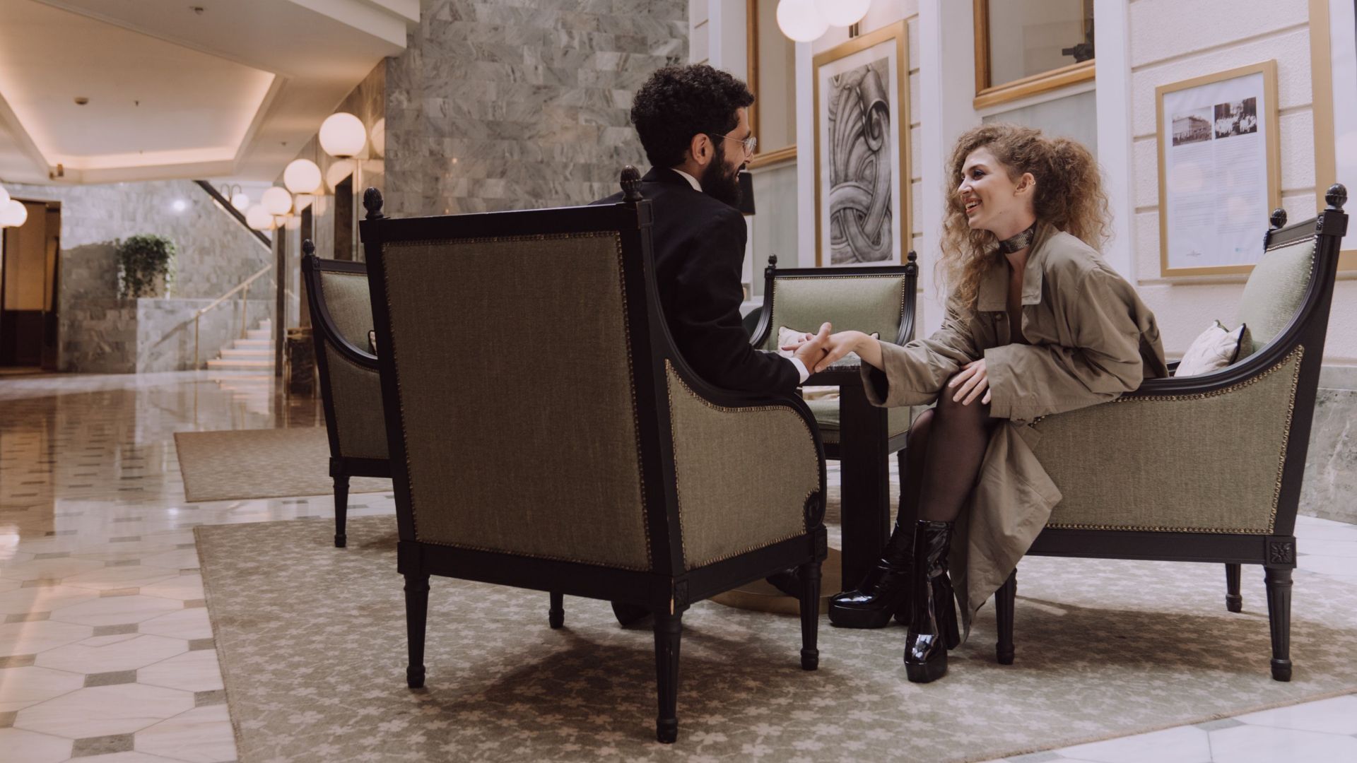 Couple sitting elegantly in a luxurious hotel lobby, exuding sophistication and style.