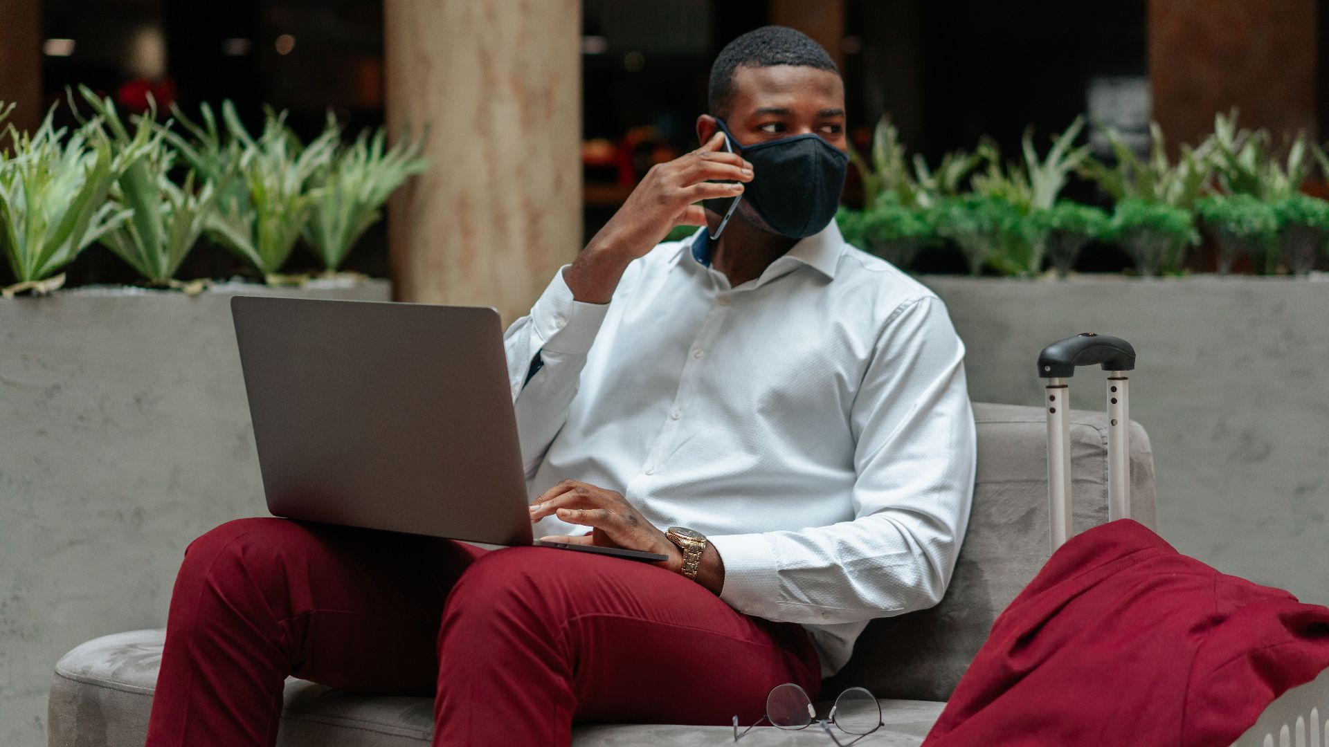 Professional man multitasks with laptop and smartphone in a modern indoor sitting area.