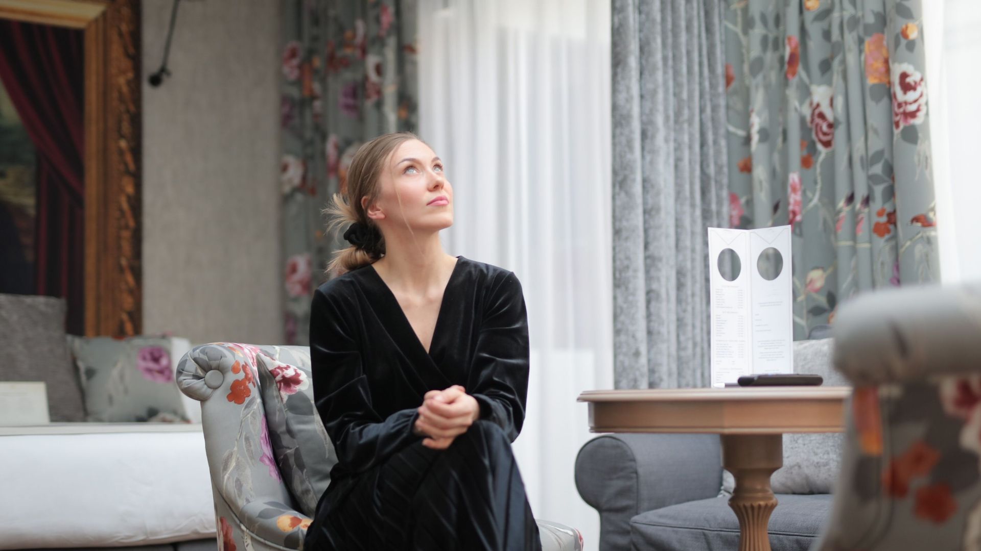 Stylish woman seated elegantly in a luxurious room, surrounded by floral decor.