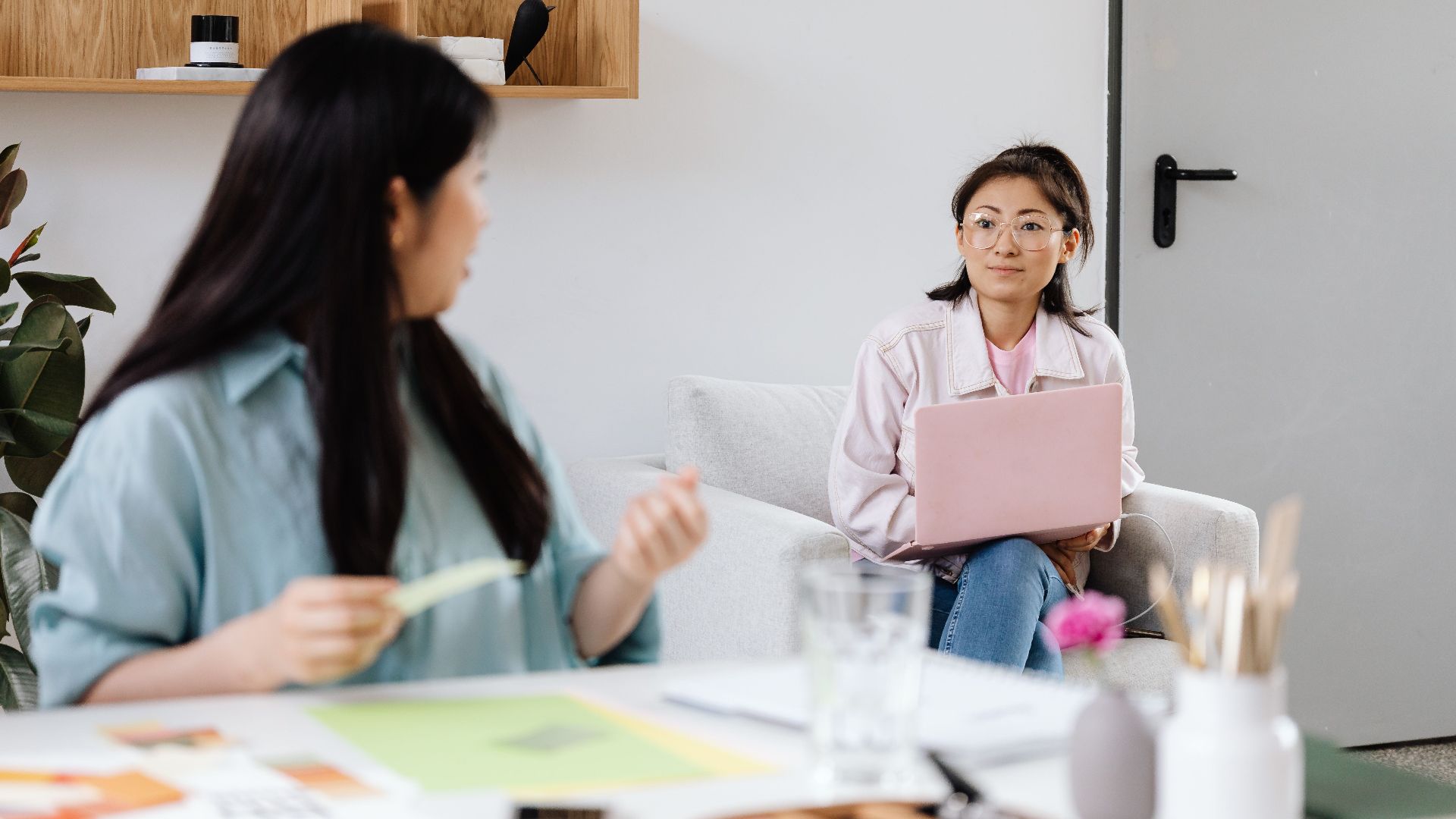 Two women engage in a discussion in a modern office setting with laptops.