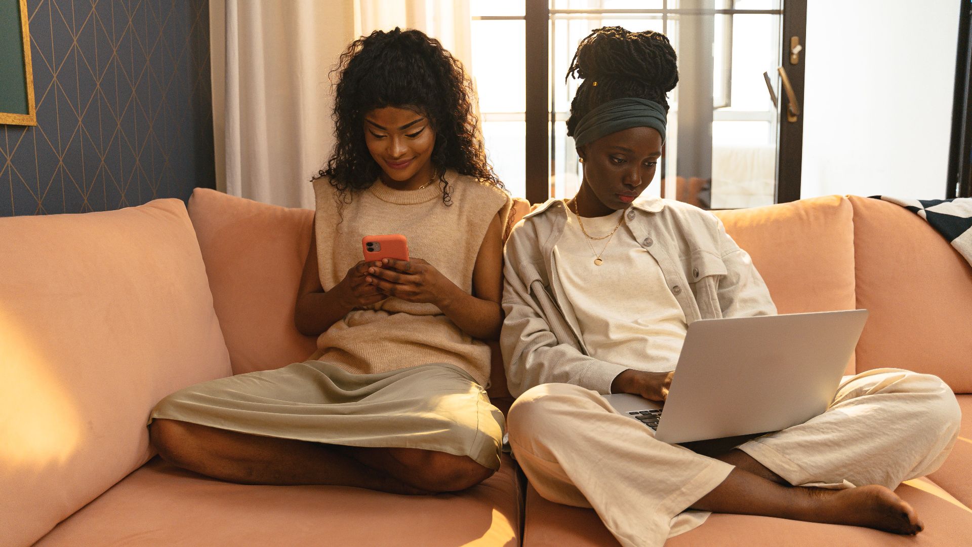 Two relaxed women using gadgets on a sofa, enjoying technology indoors.