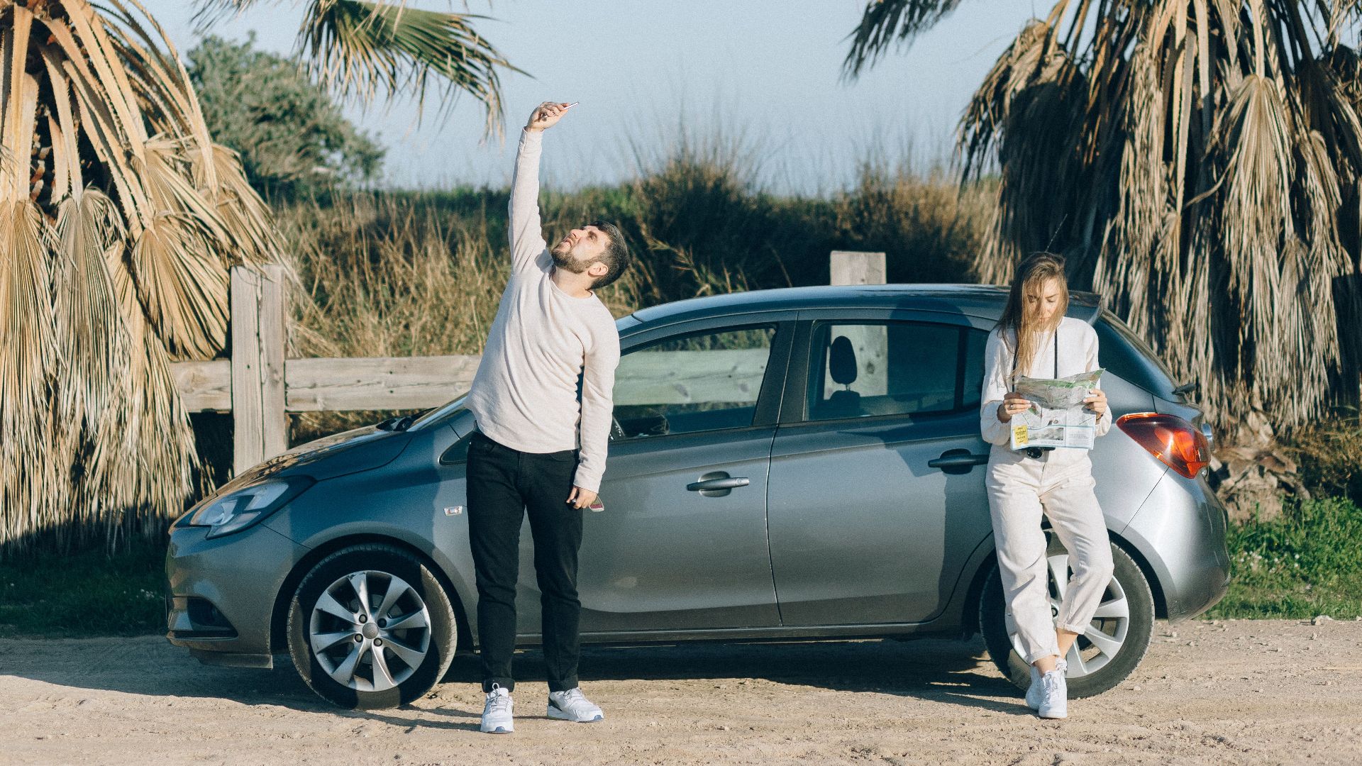 Couple on a road trip using a map near a car by palm trees on a sunny day.