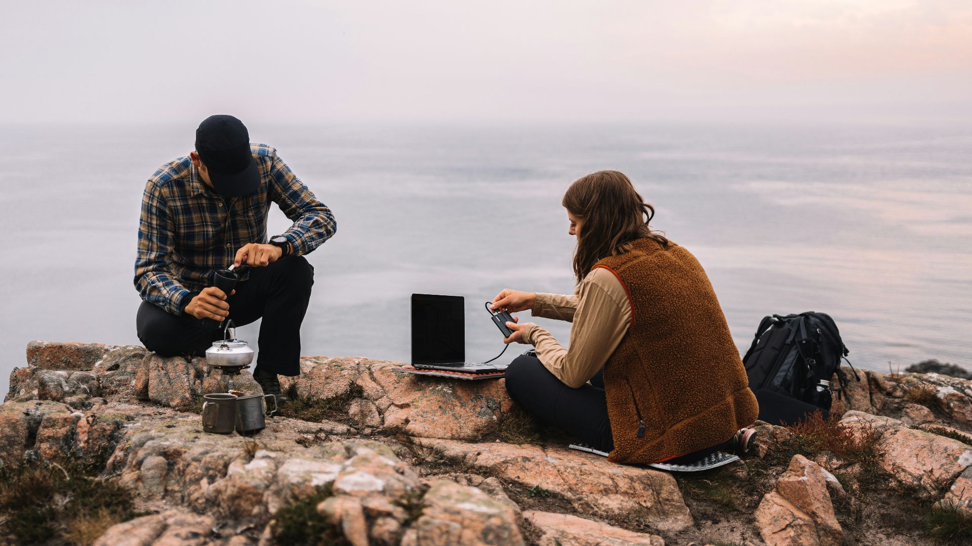 a man and woman sitting on a rock overlooking the ocean