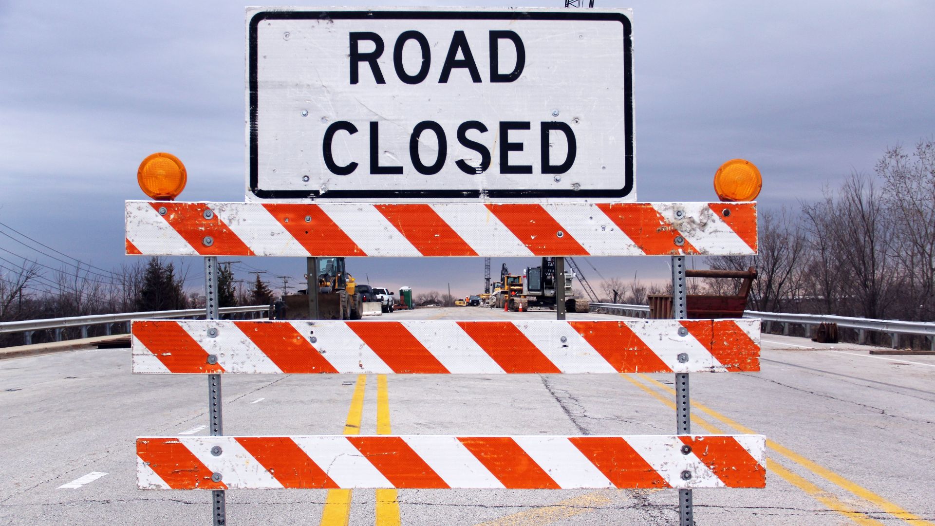 A road closed sign with barricade highlights caution on a suburban highway.