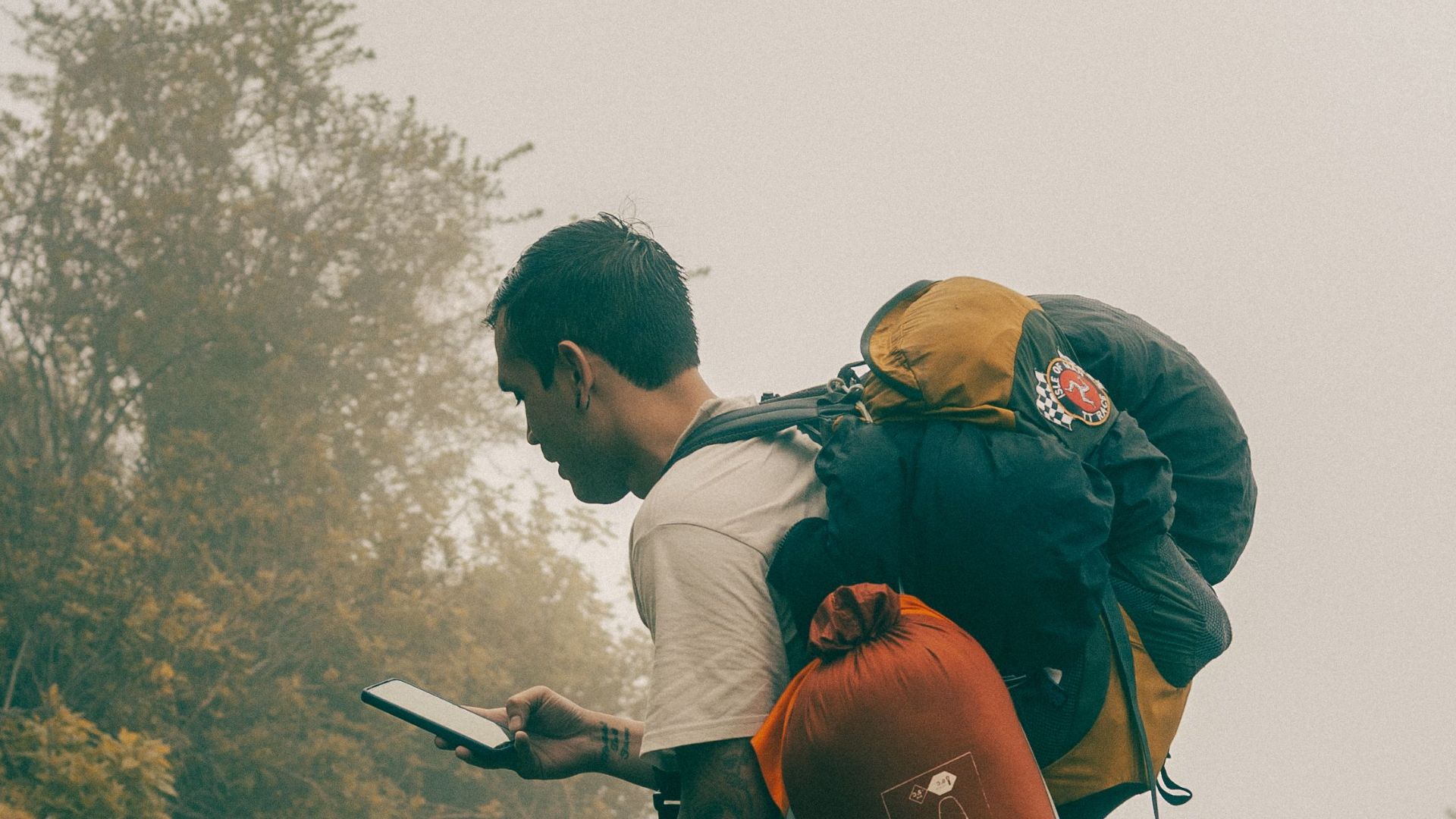 A man hiking uphill in a misty forest, using a smartphone for navigation.