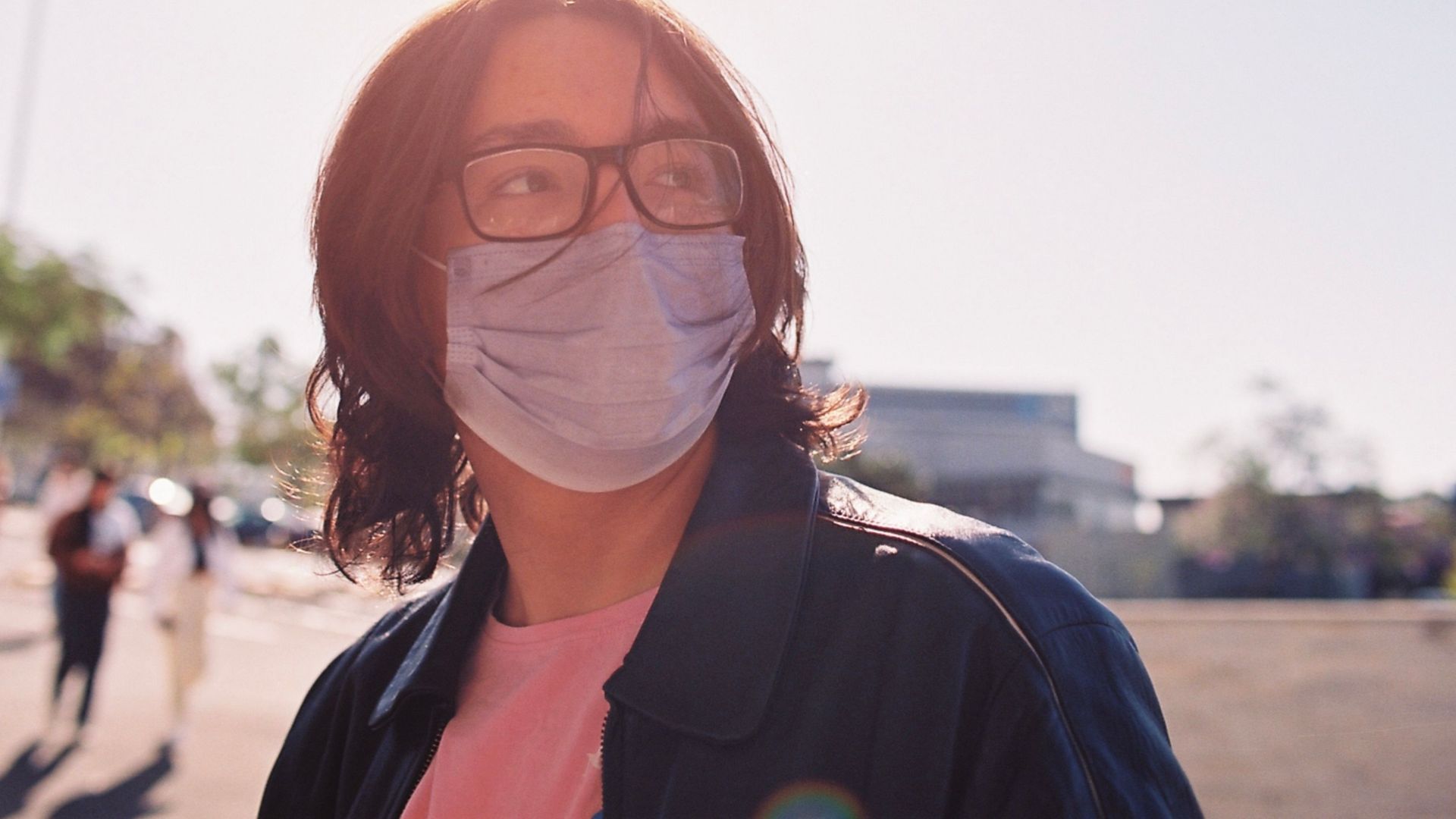 A young person with a face mask and glasses outdoors in Tlaquepaque, Mexico, under bright sunlight.