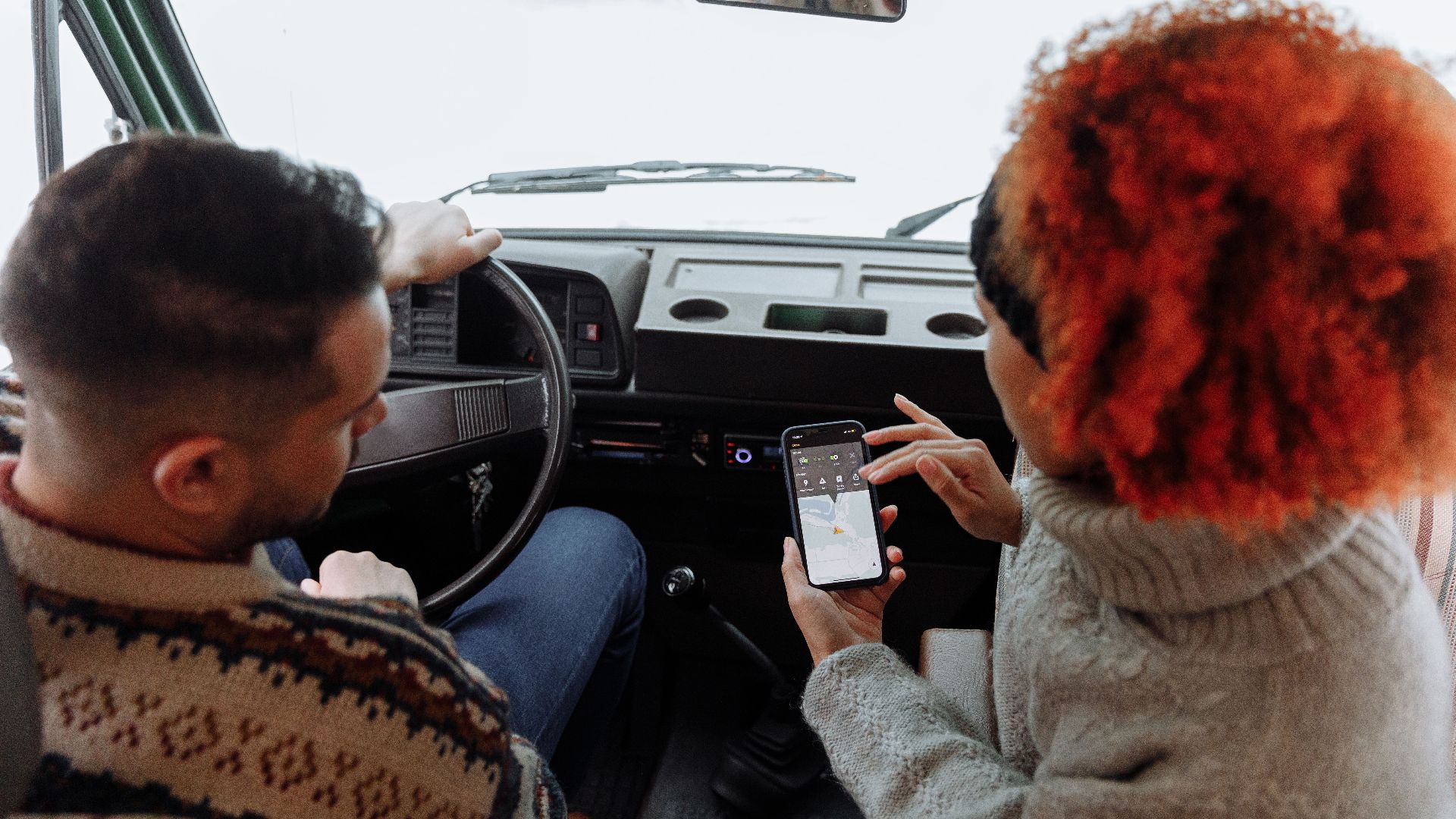 A couple using smartphone navigation while traveling in a van during winter.