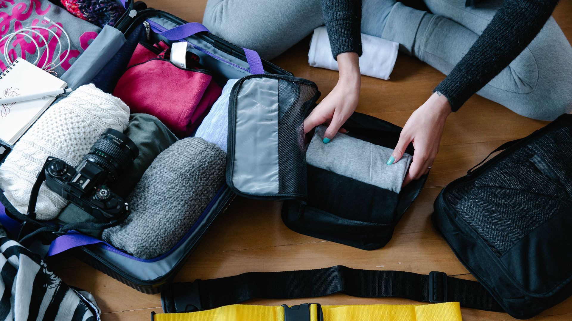 A woman arranging clothes and accessories into a suitcase, preparing for travel.