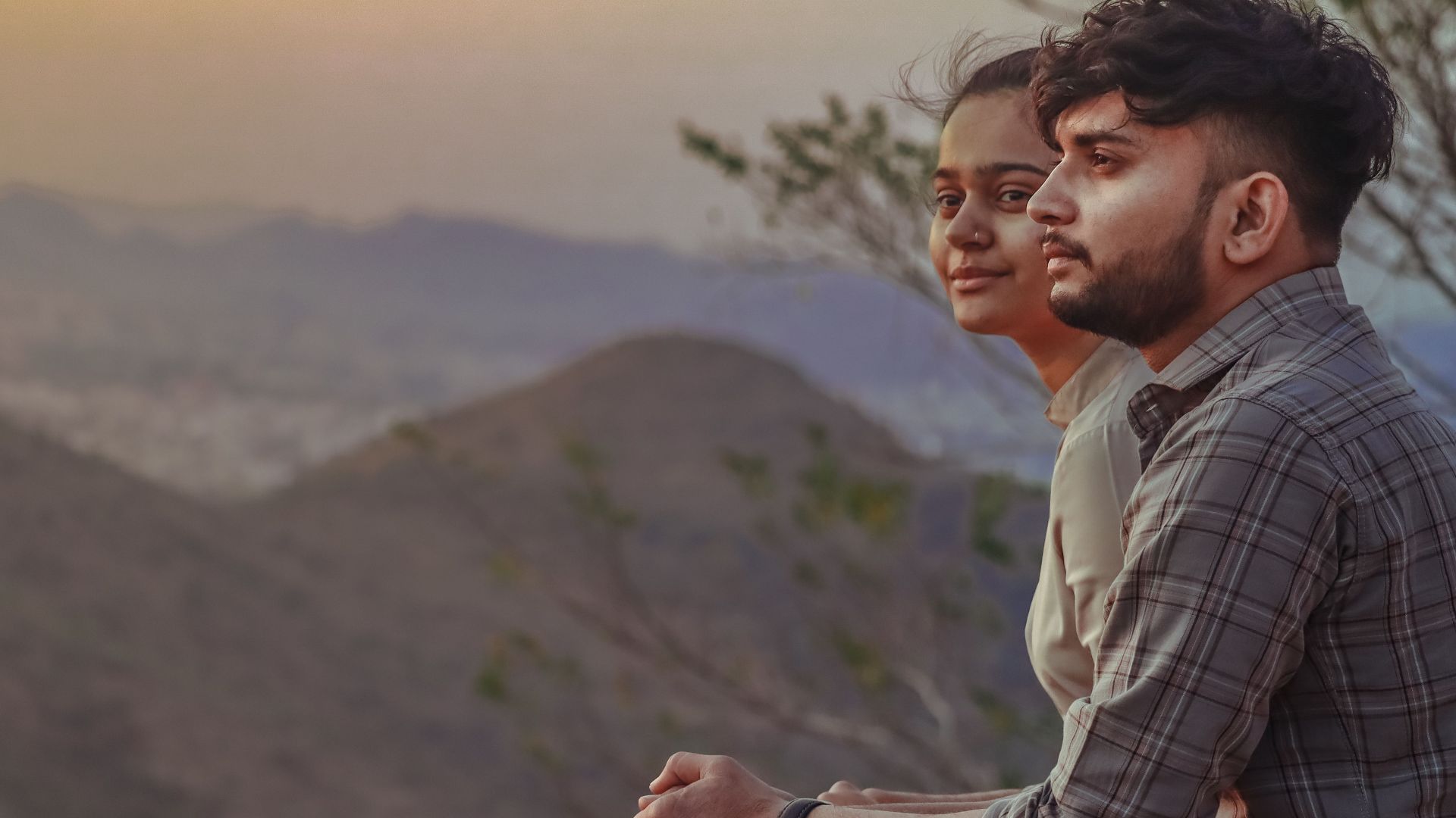 A couple enjoys a serene mountain view during sunset, creating a peaceful moment in nature.