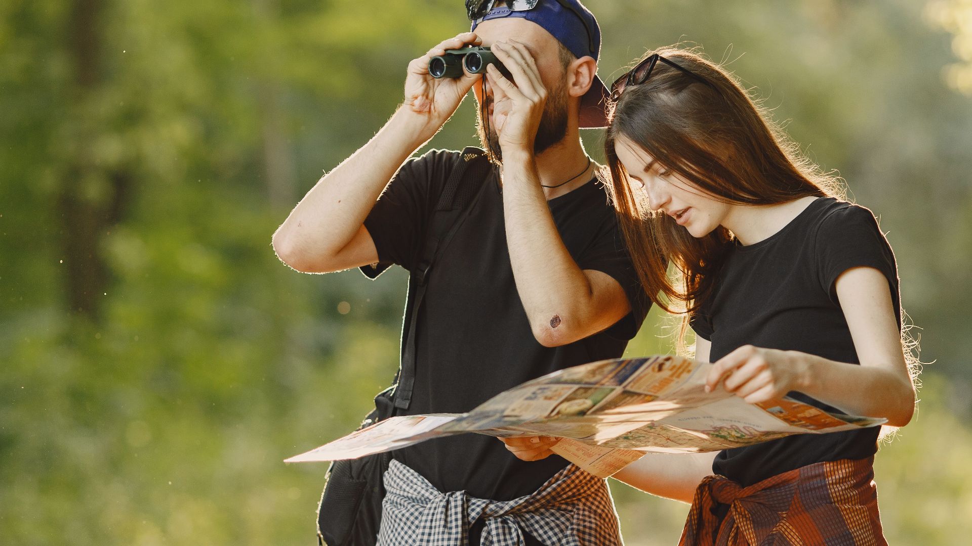 A couple outdoors using binoculars and a map for an adventure journey.