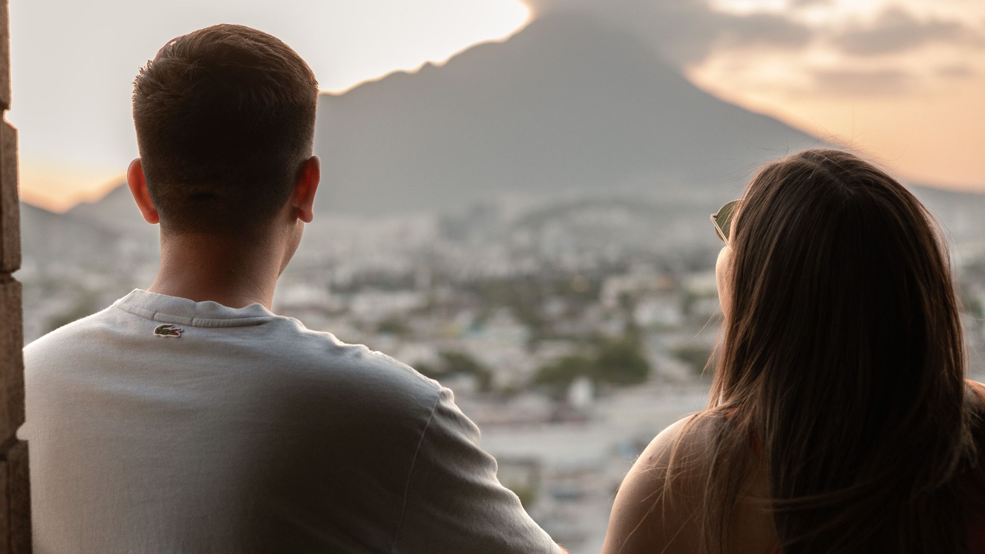 A young couple shares a romantic moment, overlooking Monterrey's cityscape and mountains at sunset.