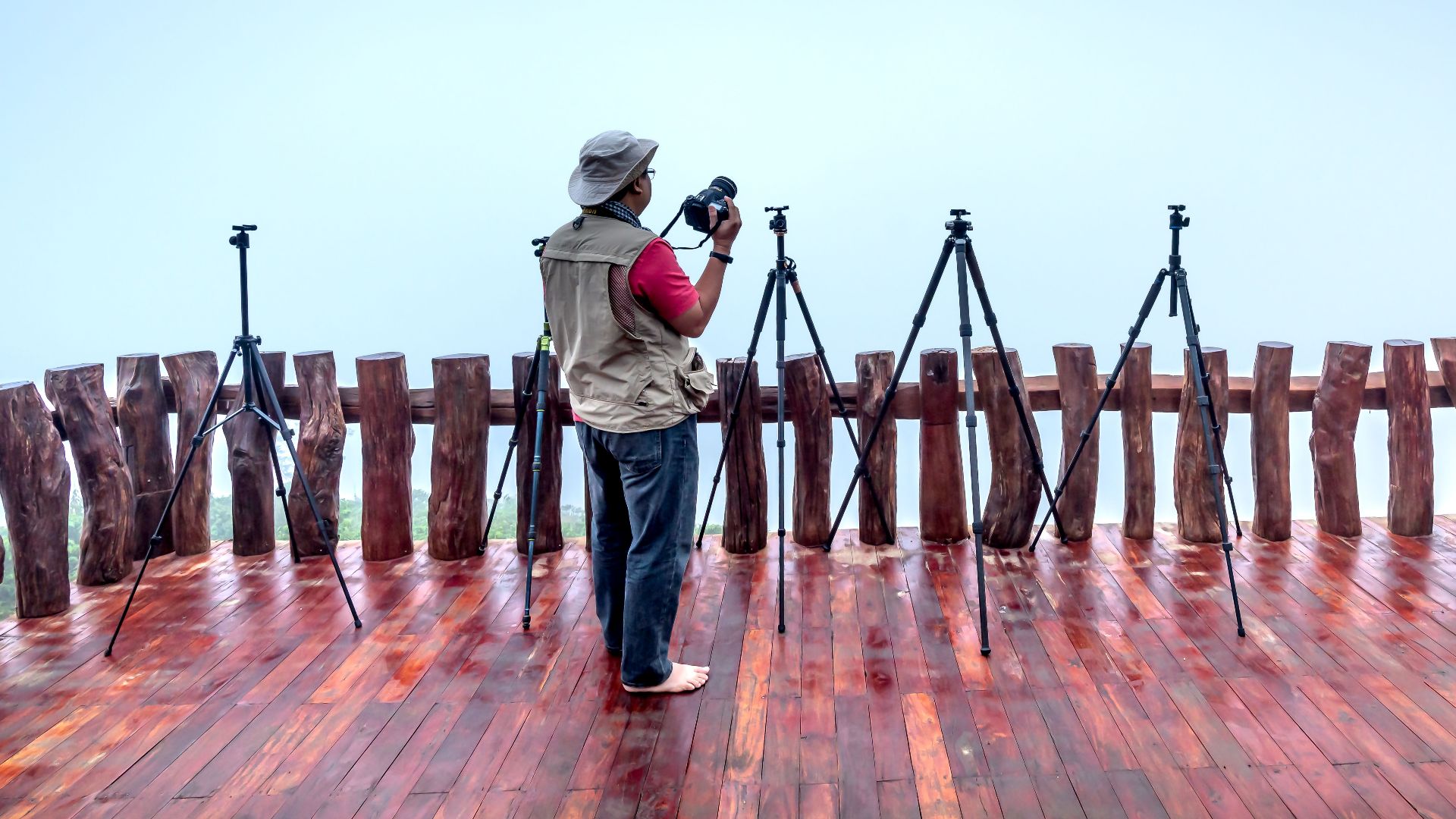 A photographer setting up tripods on a wooden terrace, prepared for outdoor shooting.
