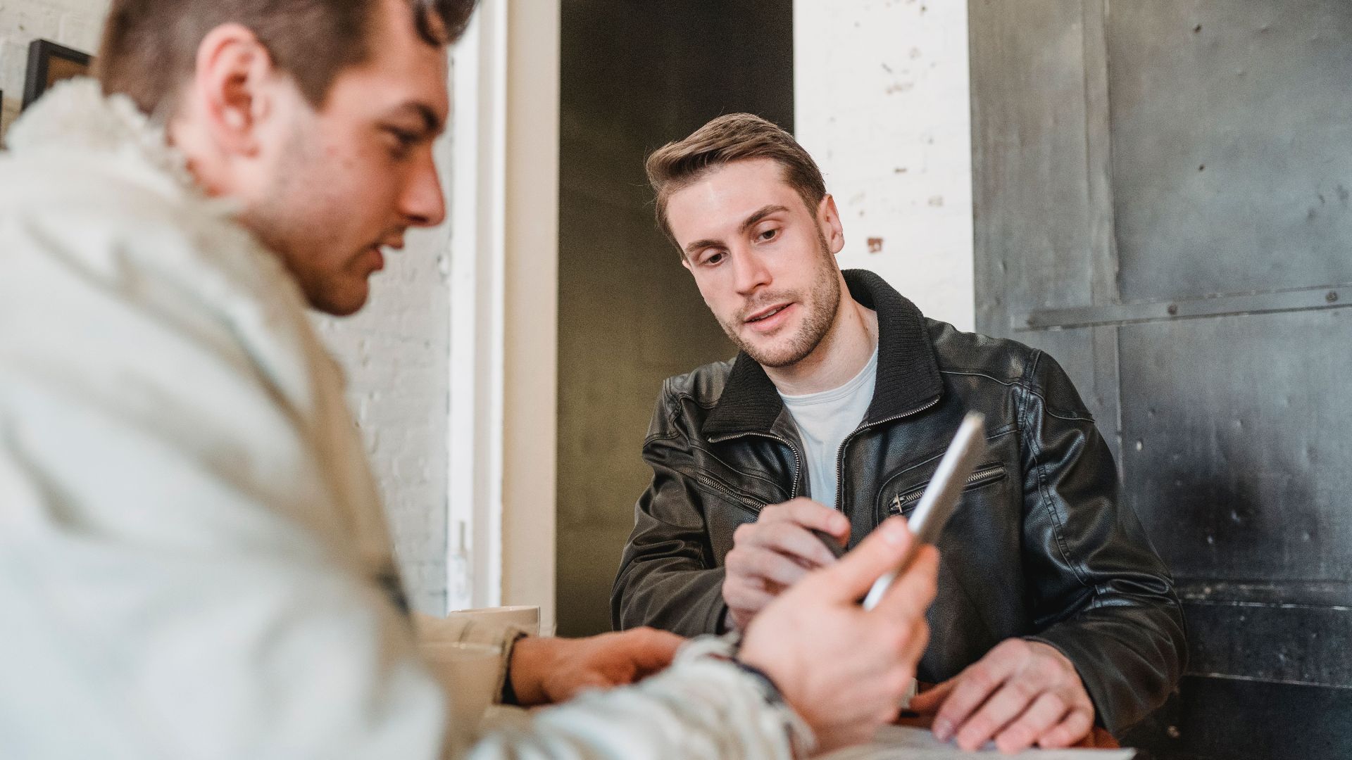 Crop colleague working with tablet while coworker in black leather jacket telling about new project