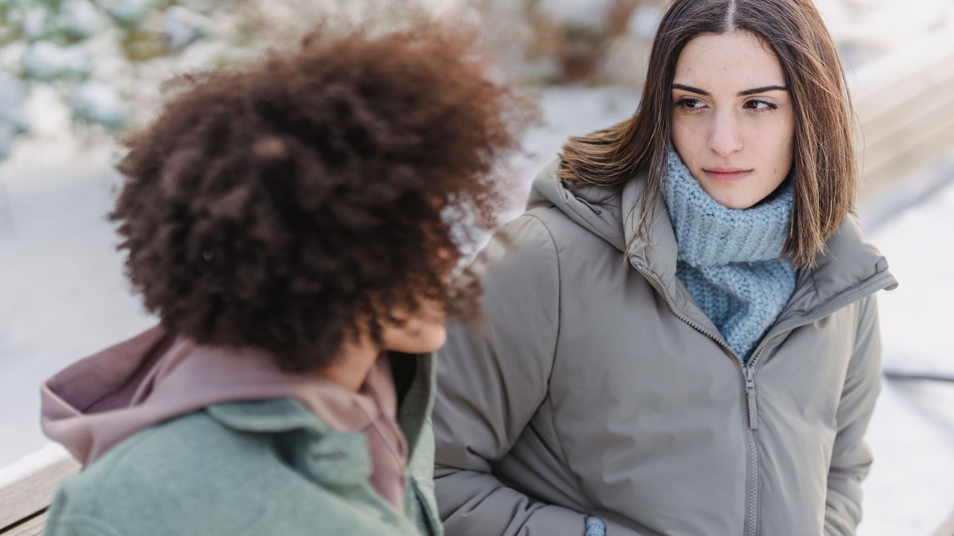High angle of crop female listening to friend while sitting on wooden bench in winter park