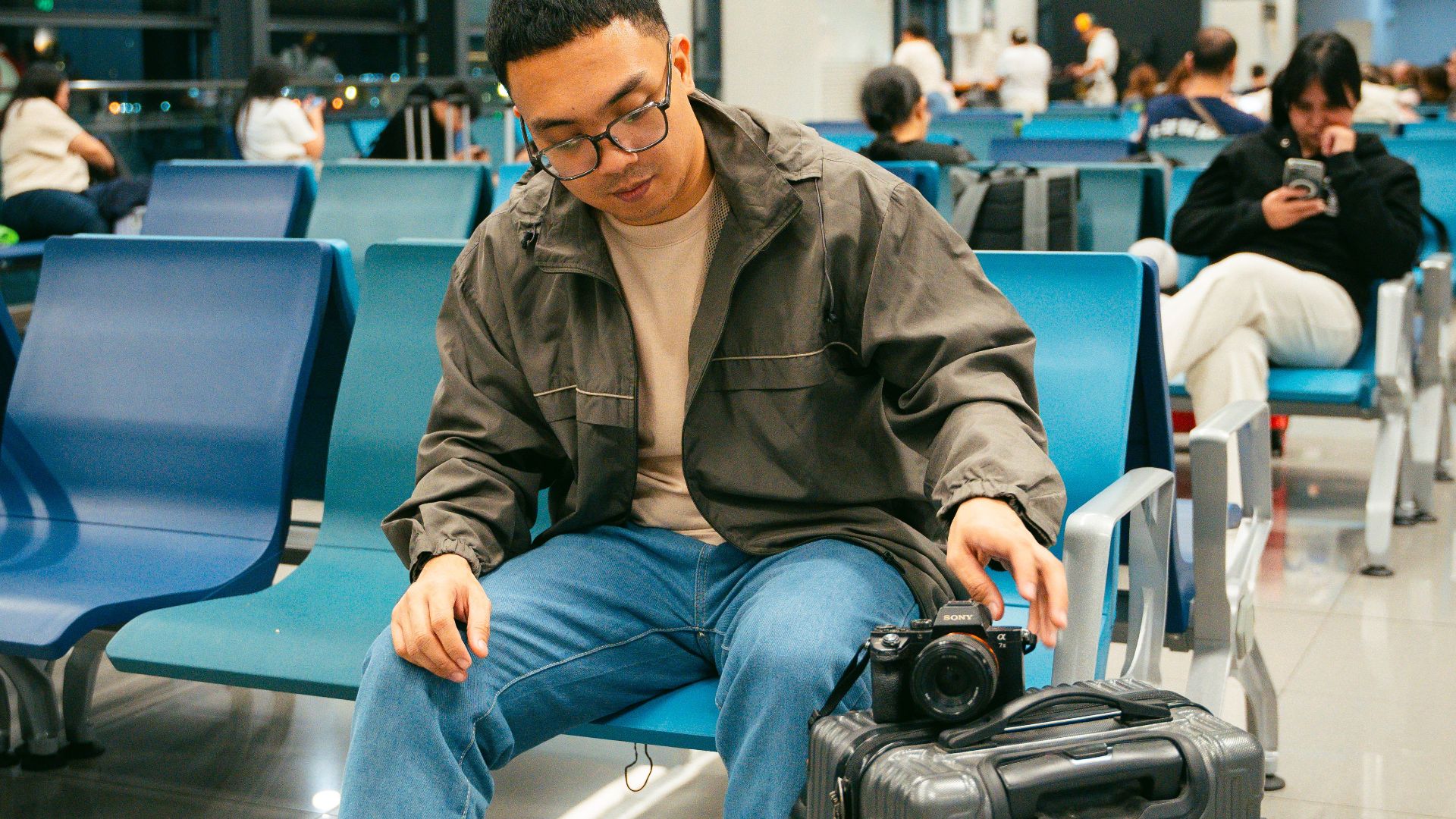 Young traveler sitting in airport terminal with luggage and camera, awaiting departure.