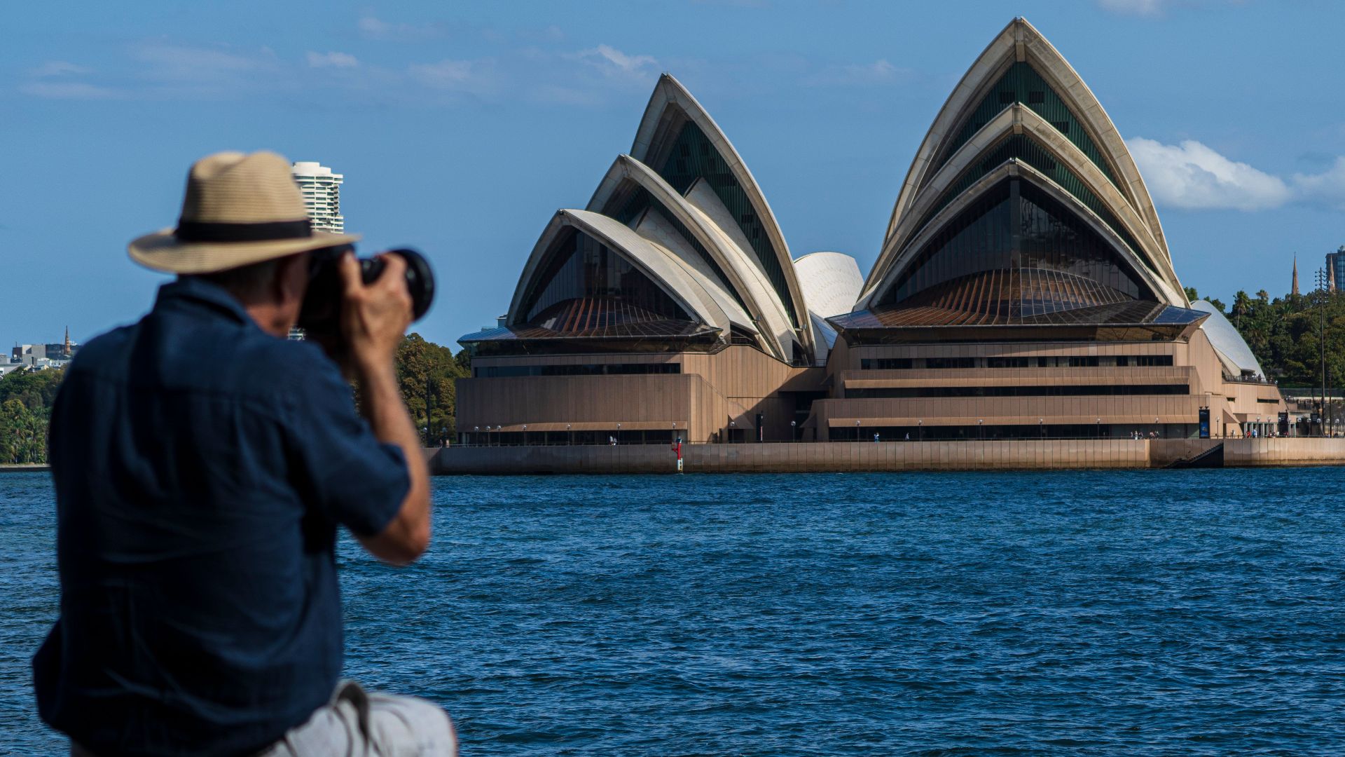 A photographer captures the iconic Sydney Opera House from across the harbor on a sunny day.