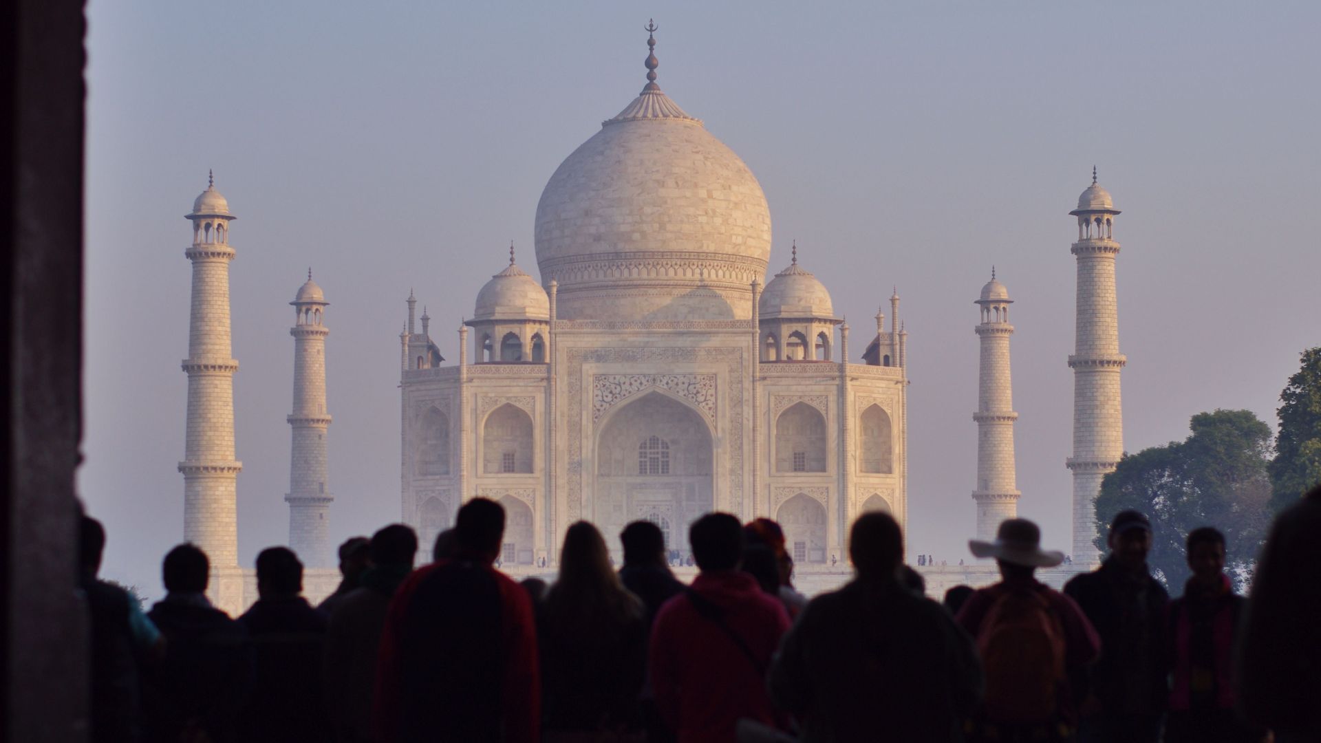 Silhouetted tourists admire the Taj Mahal's iconic beauty at sunrise, a UNESCO World Heritage site.