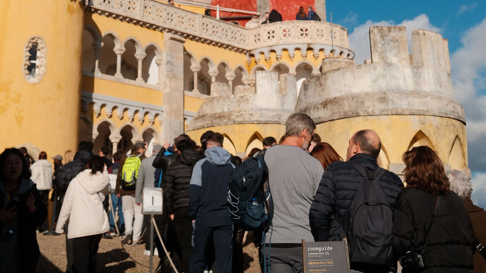 Tourists explore the vibrant Pena Palace under a bright blue sky in Sintra, Portugal.