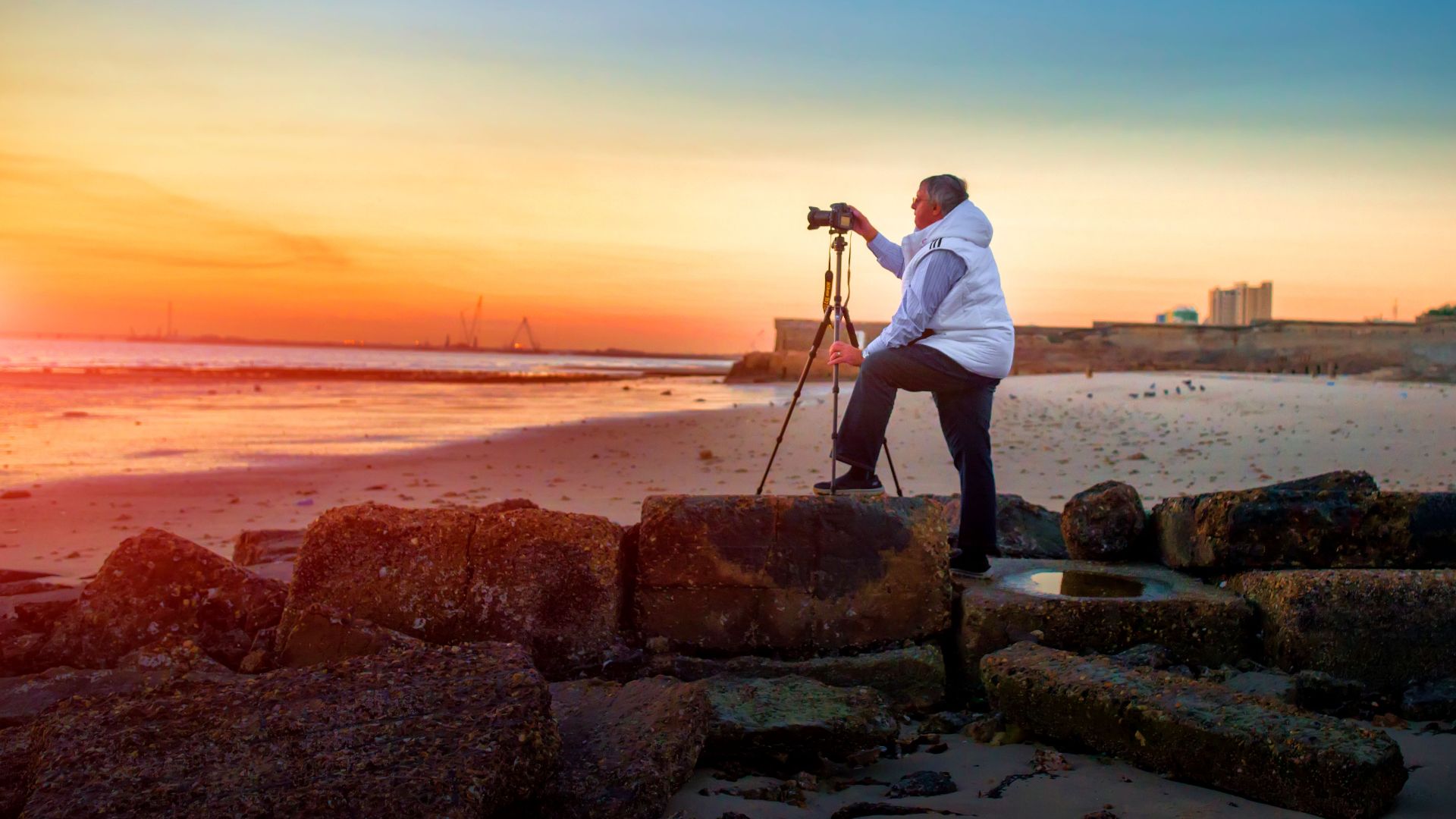 A photographer capturing the vibrant sunrise on a serene Dubai beach with a tripod and camera.