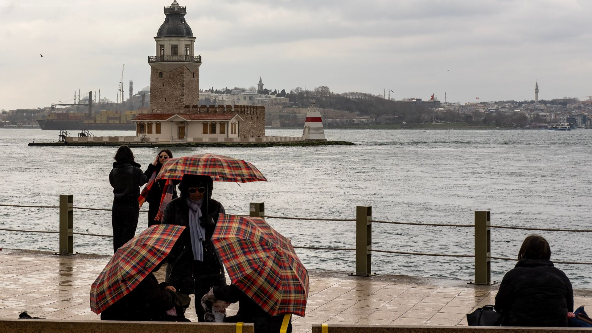 Scenic view of Maiden's Tower on a rainy day in Istanbul with people and umbrellas.