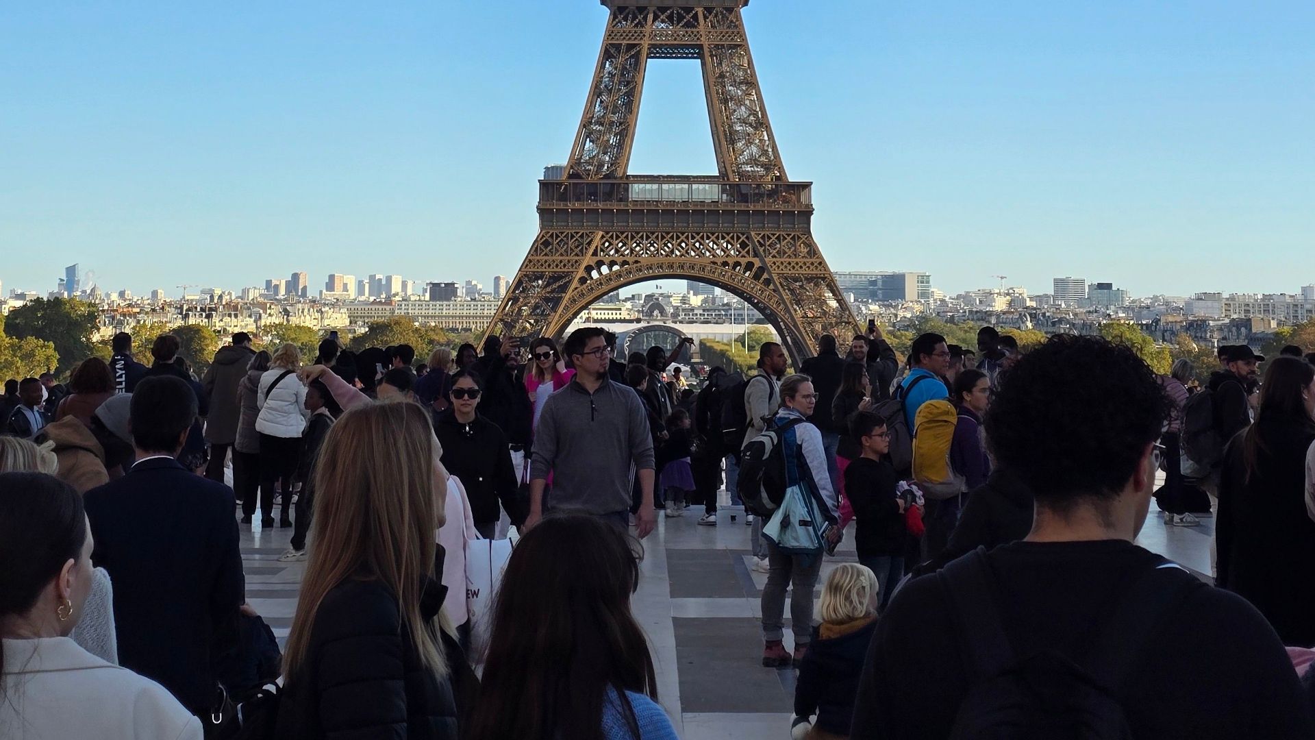 A busy day at the Eiffel Tower with crowds gathered under a vibrant blue sky.