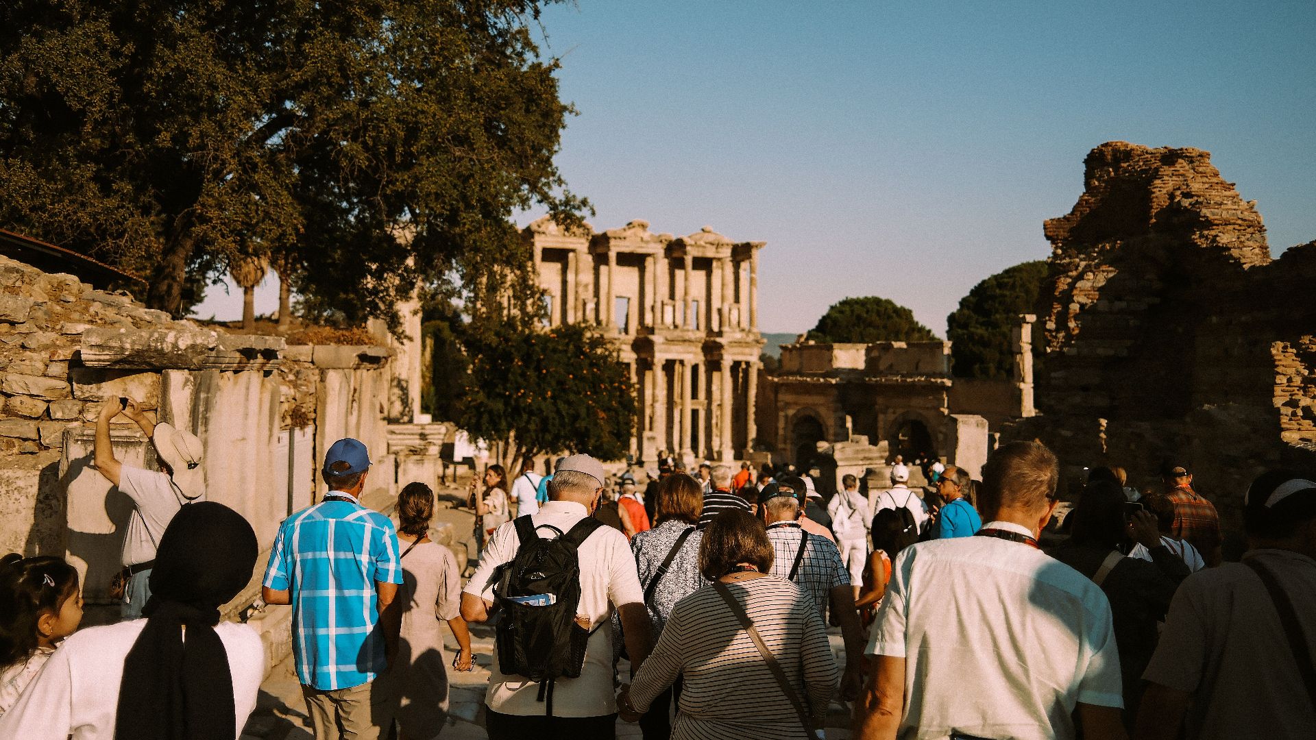 A group of tourists explore the historic ruins of Ephesus under a clear blue sky.