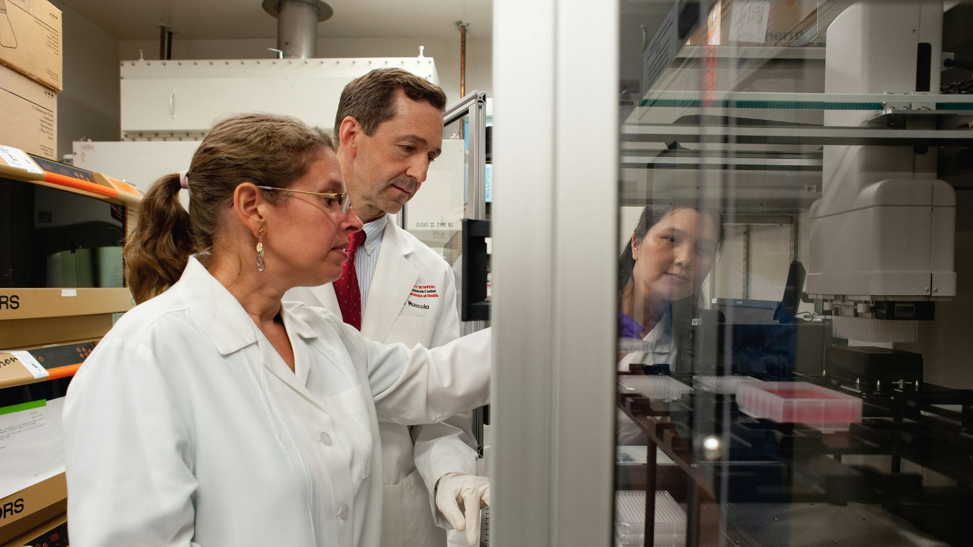 a man and a woman in lab coats looking at something in a cabinet