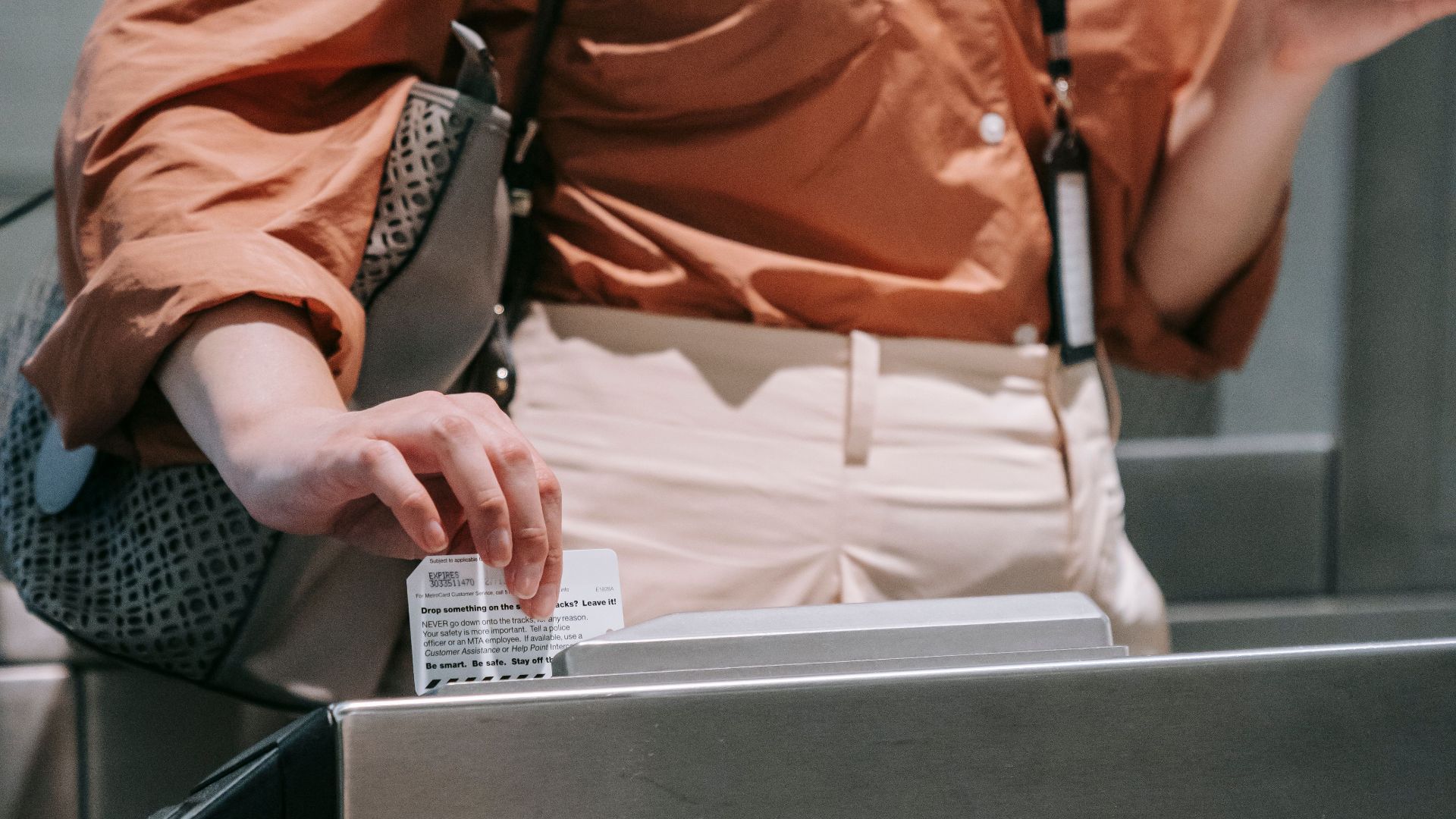 Woman swipes card at subway turnstile, holding coffee to-go. Urban transit scene.