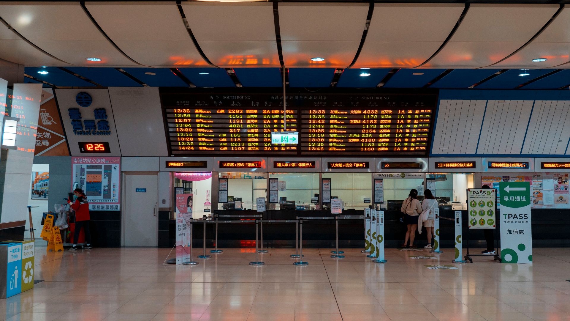 Interior of a train station with a digital timetable and ticket counters.