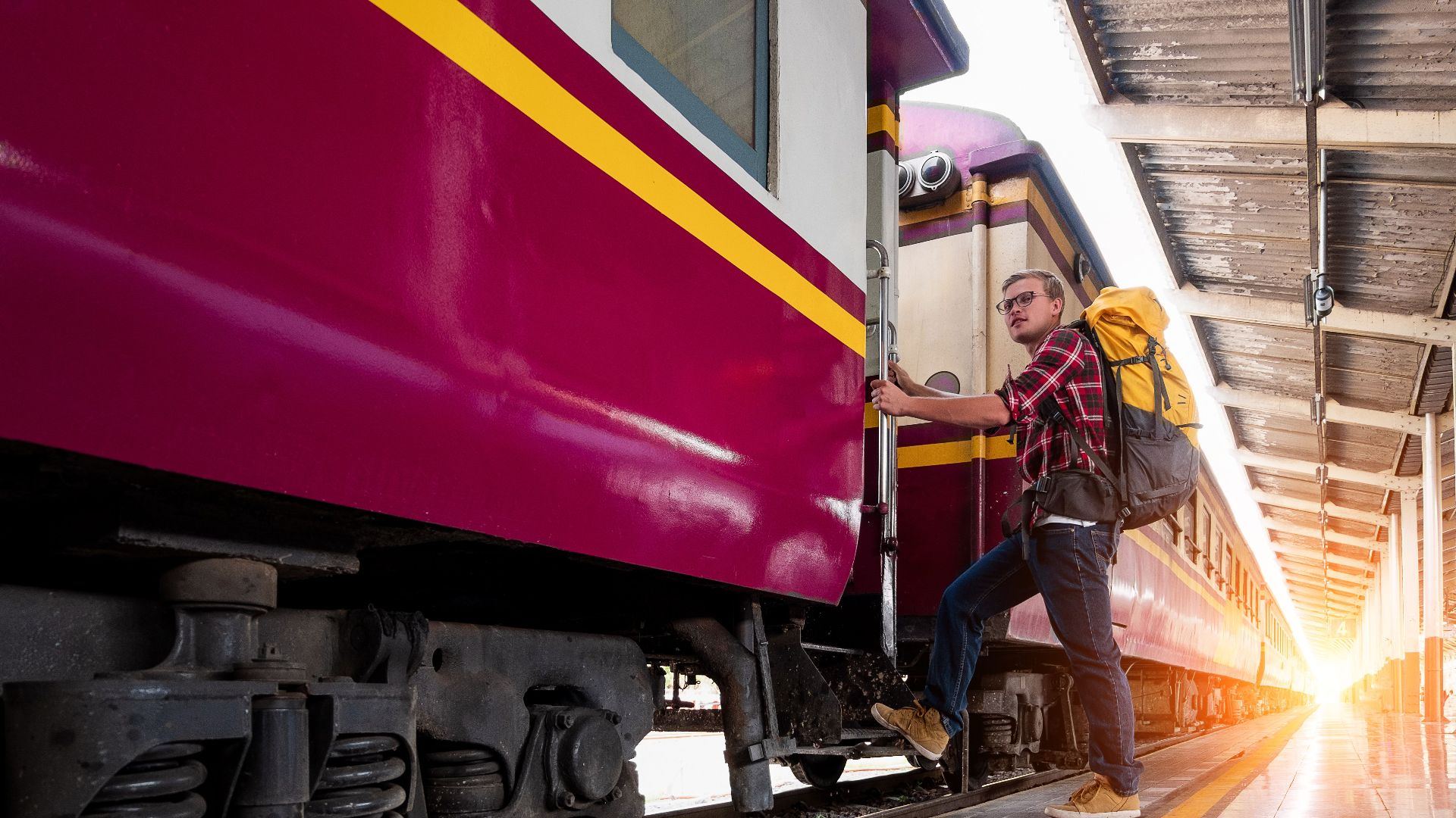 Man with backpack boarding a train at urban railway station during daytime travel adventure.
