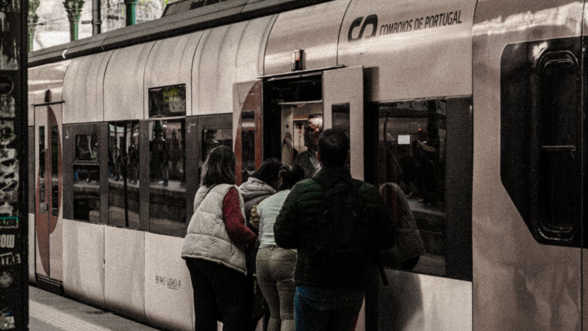 People boarding a train at a covered railway station platform in daylight.