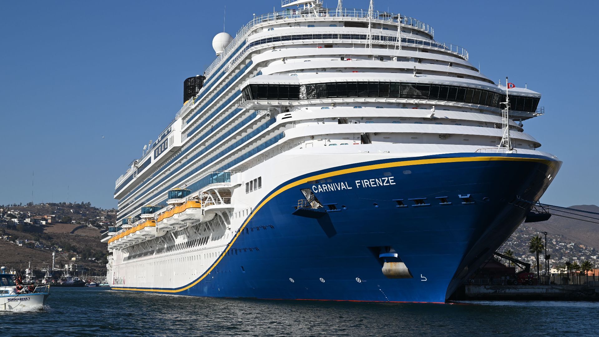 Close-up view of a large cruise ship docked at a port under a clear blue sky with visible cityscape.