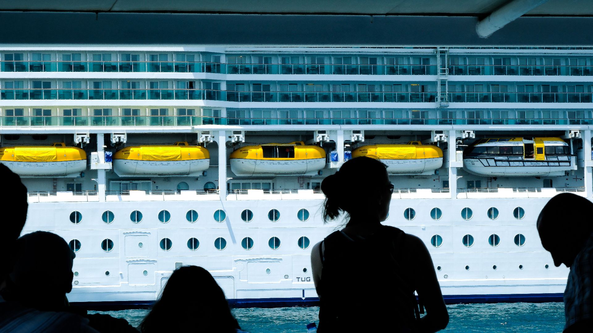Silhouettes of people observing a large cruise ship from a dock in Türkiye.