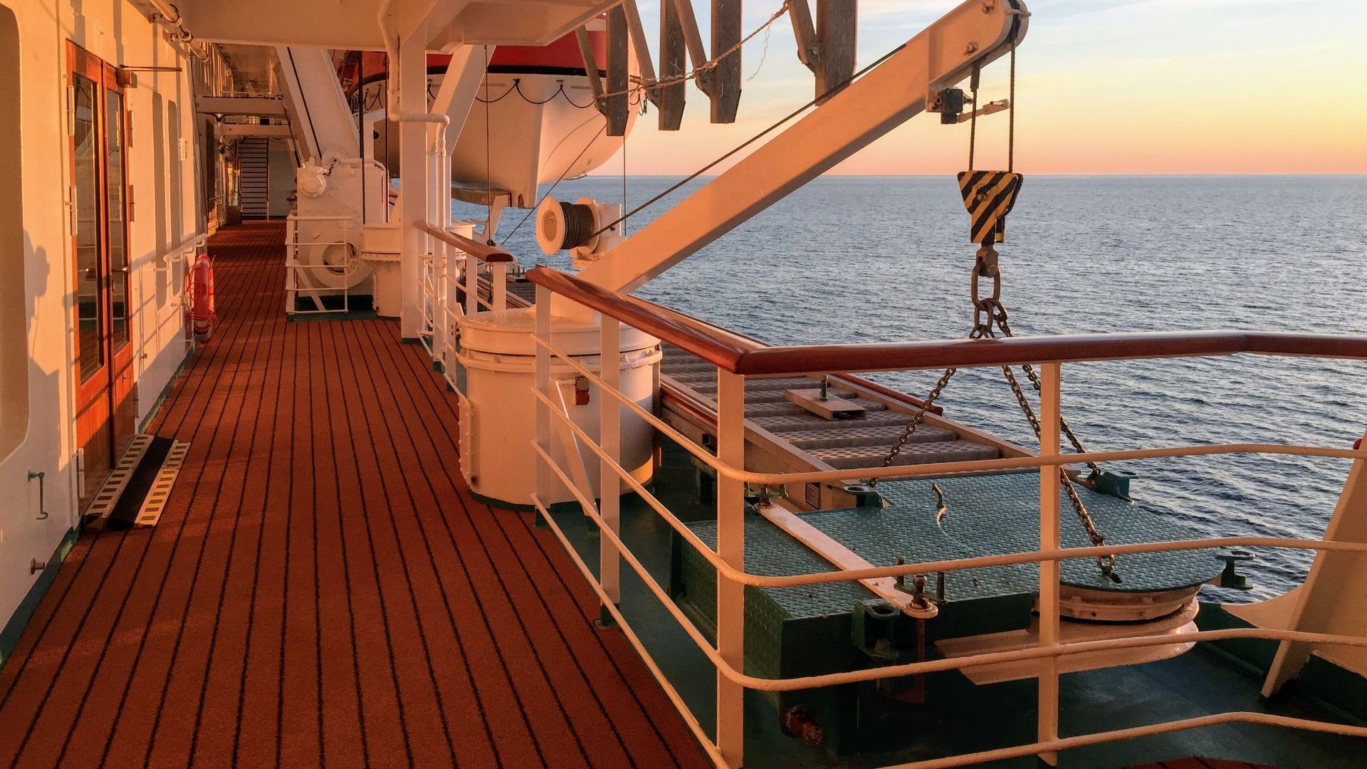 A serene view of the promenade deck on a cruise ship at sunset, overlooking the ocean.