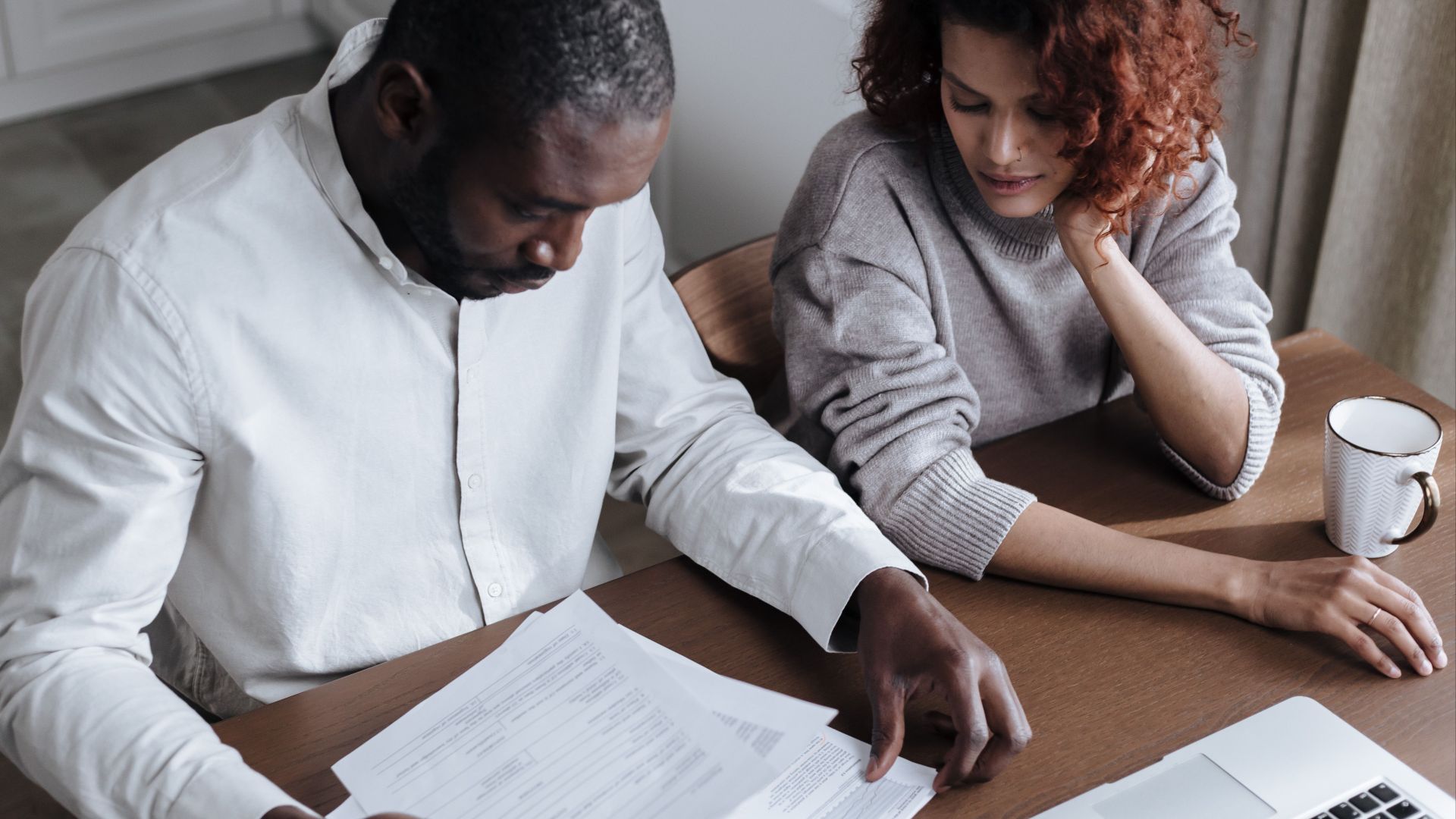 A couple reviews important documents together at a home desk with a laptop.