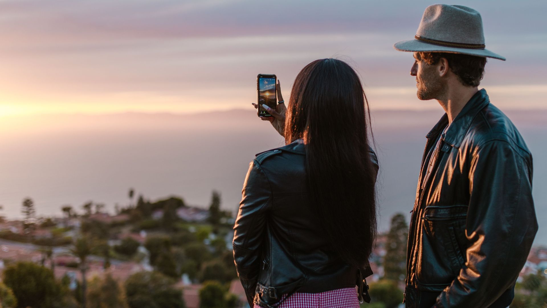 Couple capturing a beautiful ocean sunset on a smartphone while traveling.