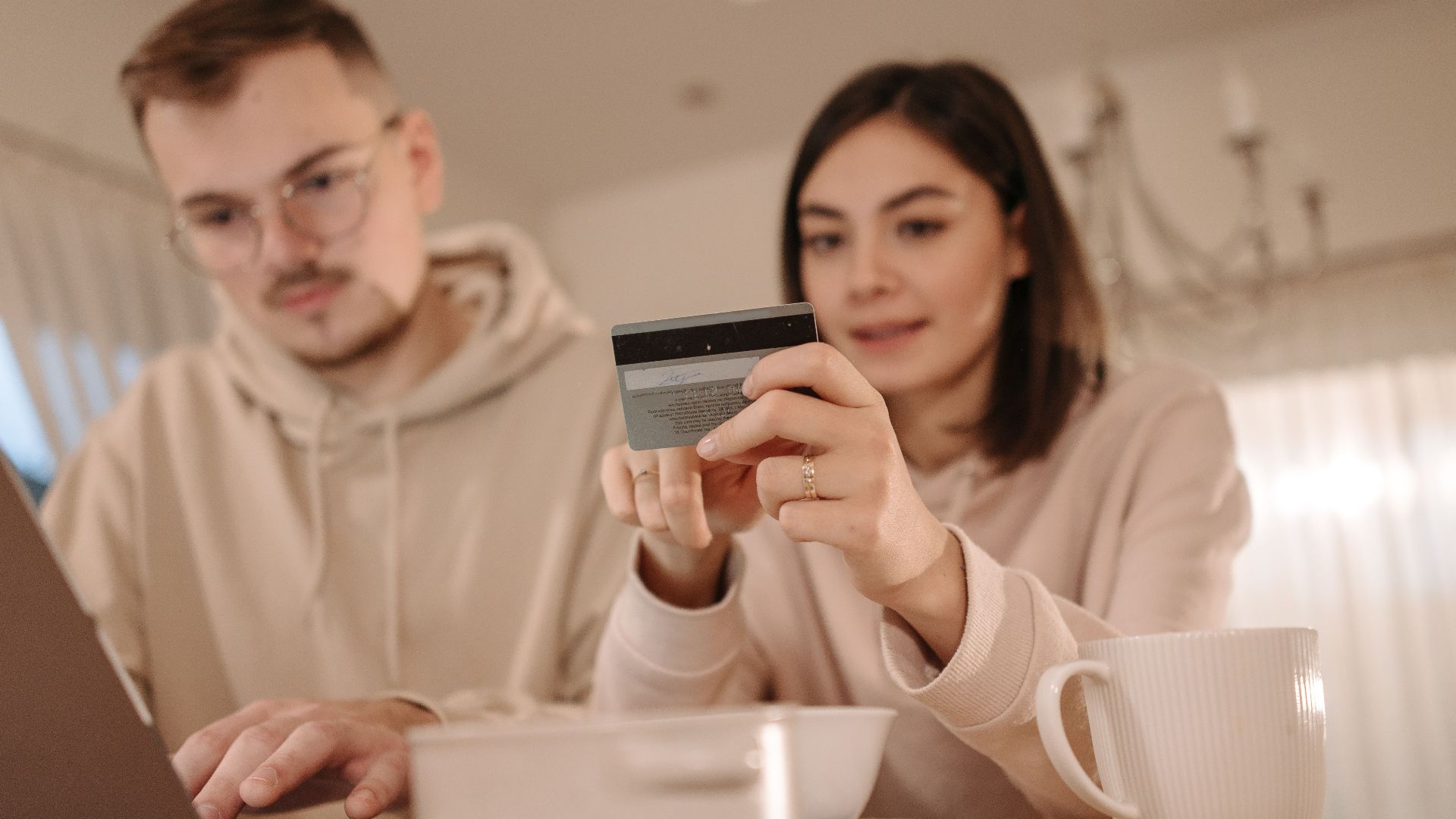 Young couple shopping online using a laptop and credit card at home, enjoying a cozy indoor setting.