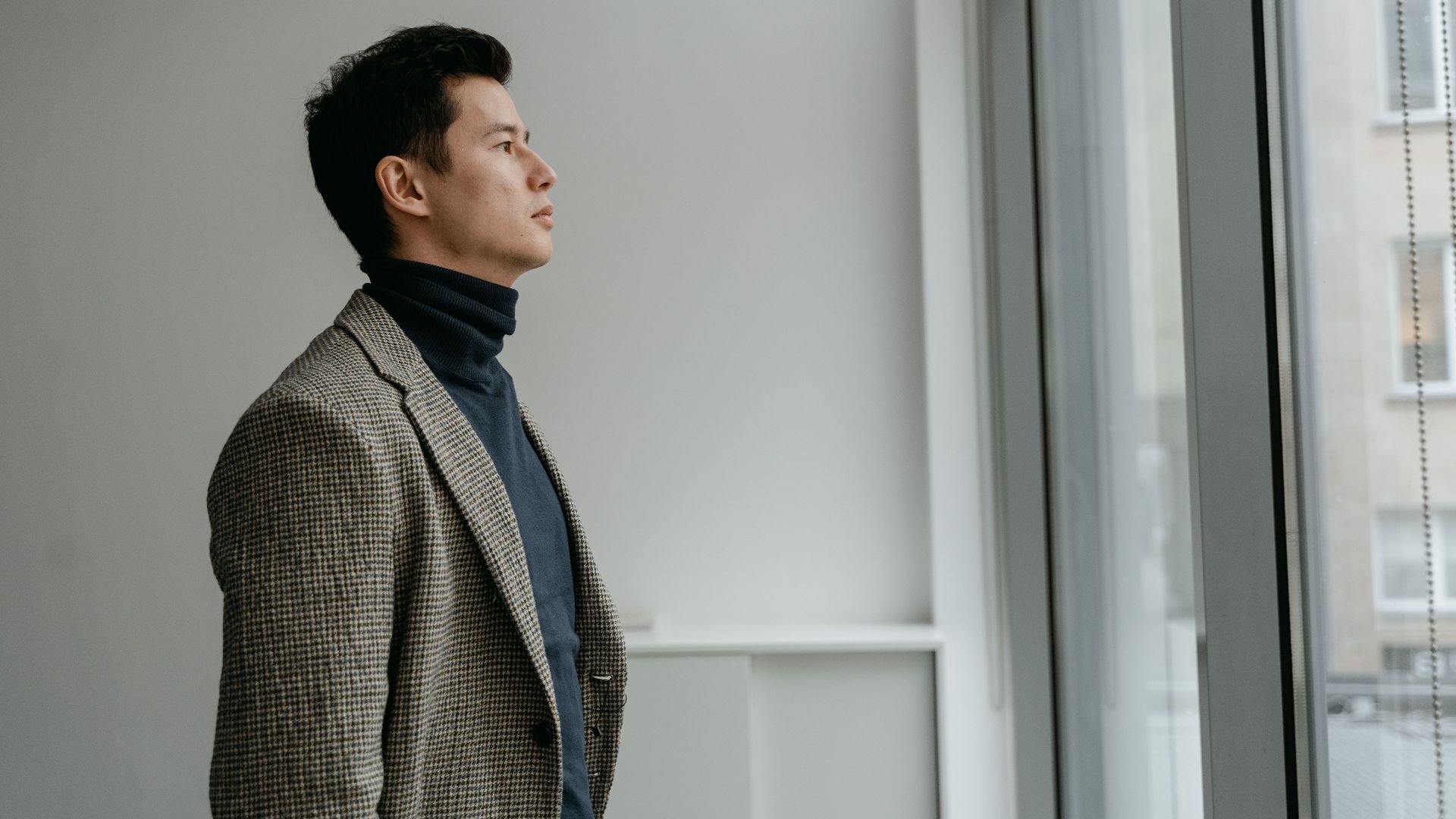 Portrait of a man in a turtleneck gazing through a glass window in a modern interior setting.
