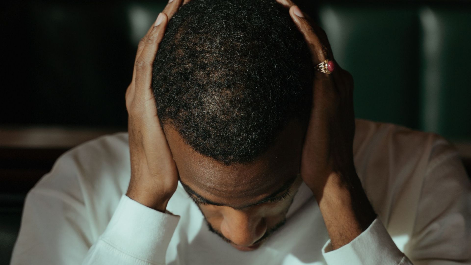 Pensive man in a white sweater inside, contemplating with hands on head.