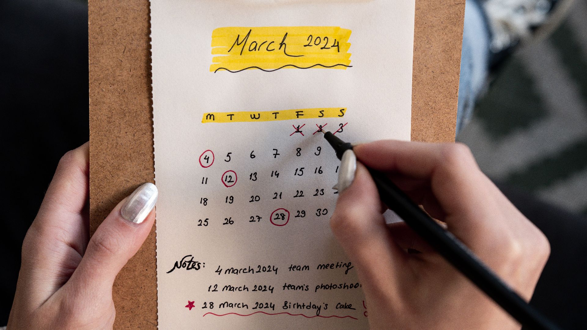 Close-up of a woman's hands organizing a planner for March 2024 with handwritten notes and highlights.