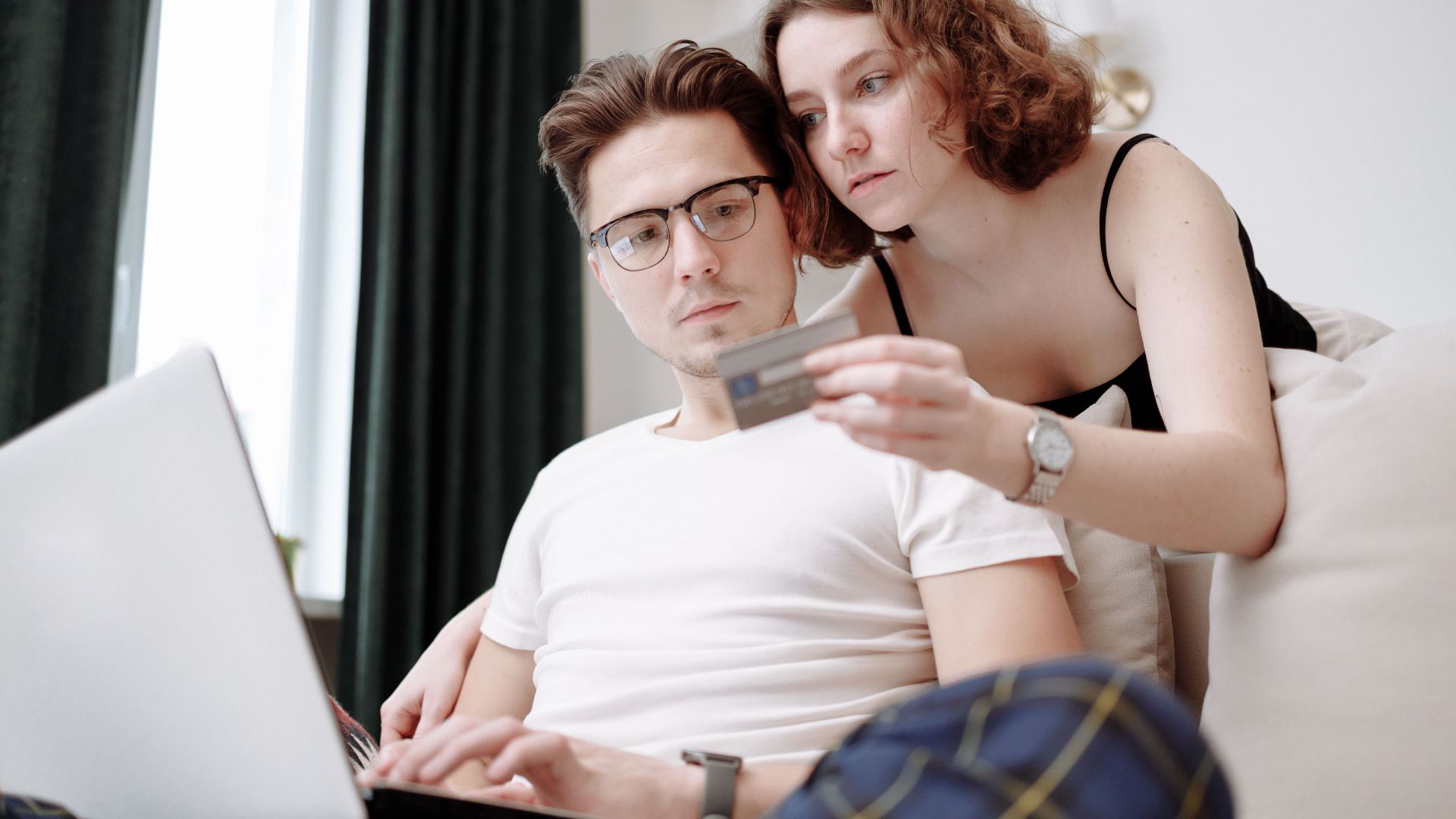 A young couple using a laptop and credit card for online shopping indoors.