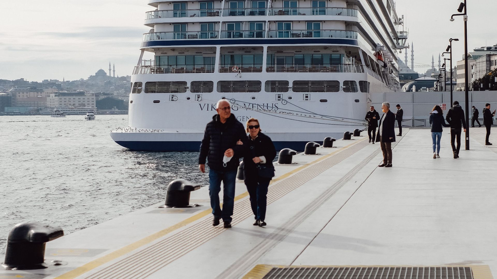 A majestic cruise ship docked at İstanbul harbor with tourists walking along the promenade.