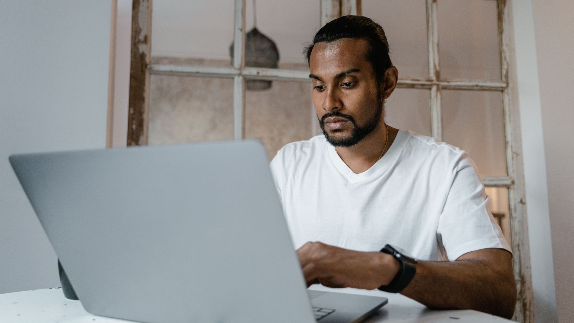 A focused man working on a laptop indoors, emphasizing productivity and concentration.