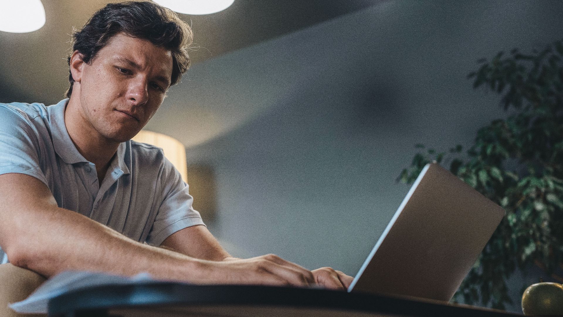 Adult man concentrating while working on a laptop indoors, in a modern office setting.
